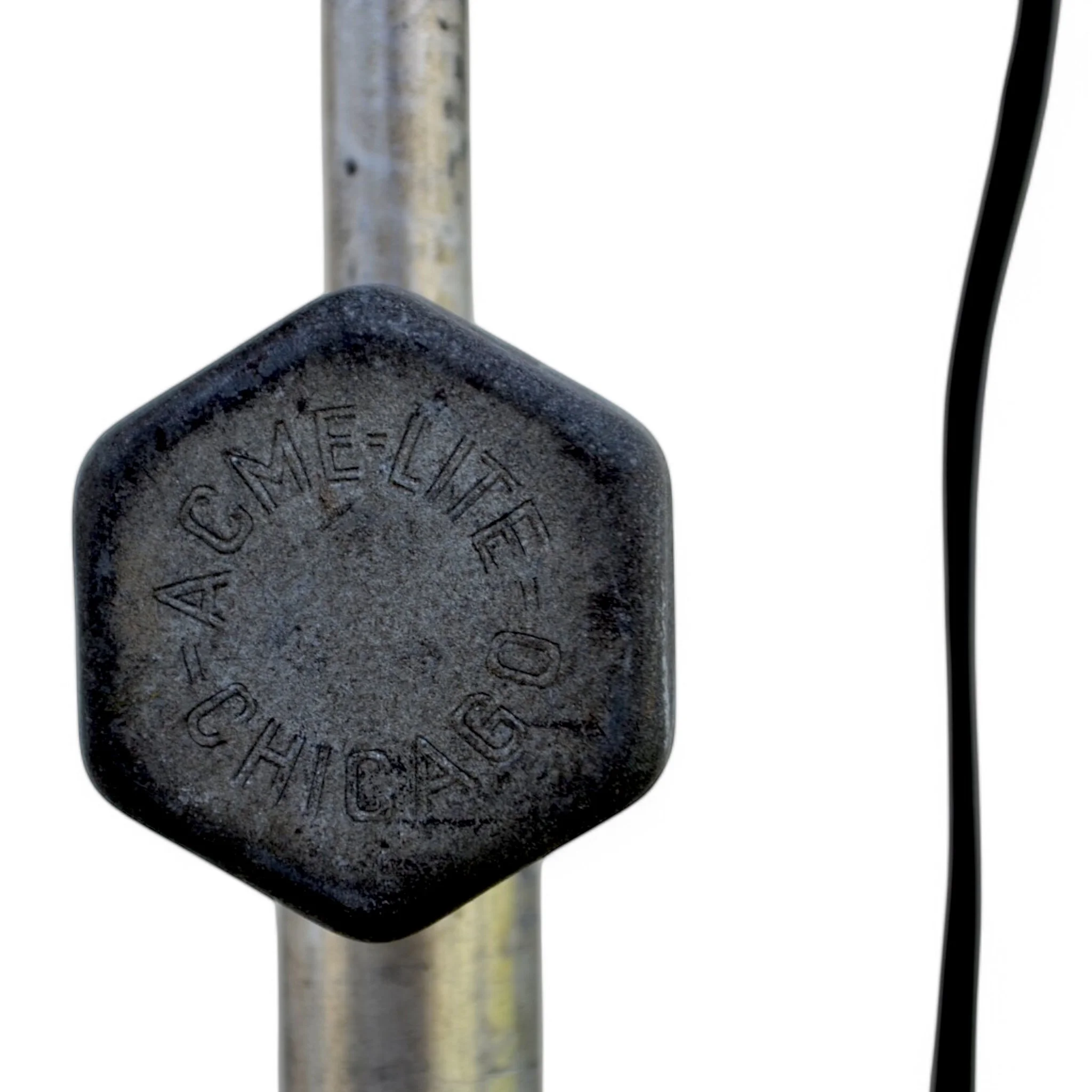 A vintage all original theater stage spotlight by Cycon, manufactured in Los Angeles, CA on a Acme Lite black metal adjustable tripod lamp in front of an industrial building.