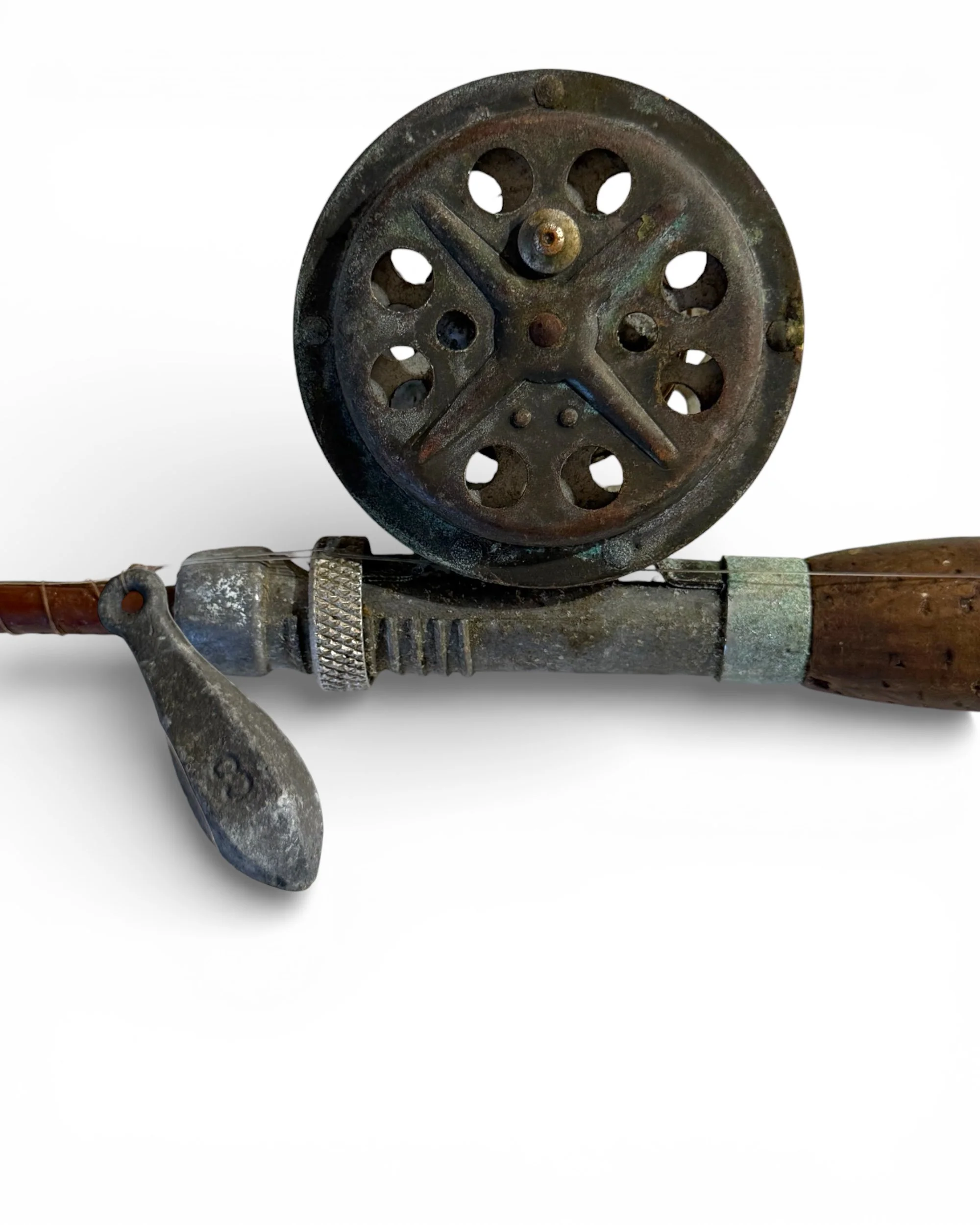 An antique fishing rod and reel. The reel is round with multiple holes and a tarnished, aged appearance. The rod is brown with a metal handle and a cork grip.