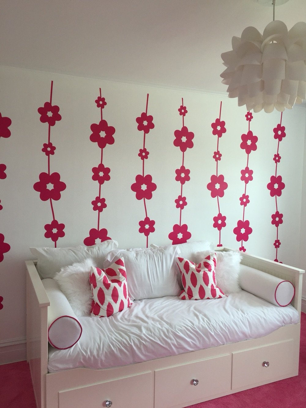 Chain of daisy wall decals in pink on a white wall behind a white day bed in a retro bedroom.