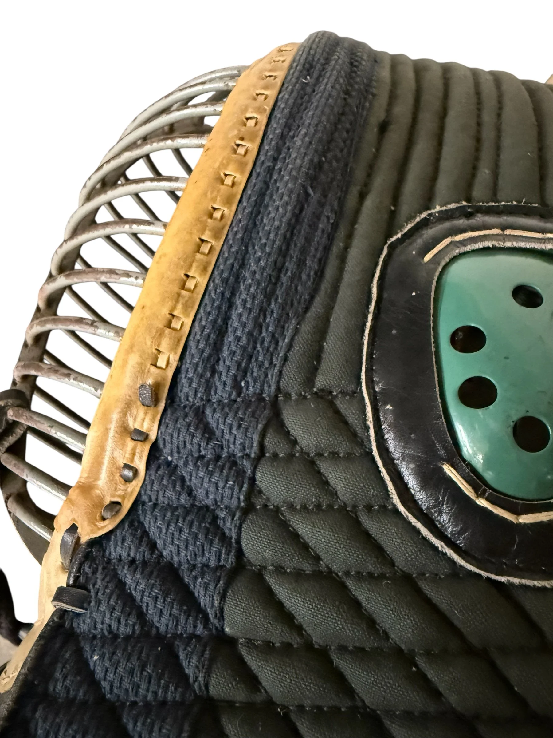 Close up detailed view of materials on a vintage 1950s Kendo men mask, including steel face guard, leather trim, metal ear guard, and quilted cotton fabric.