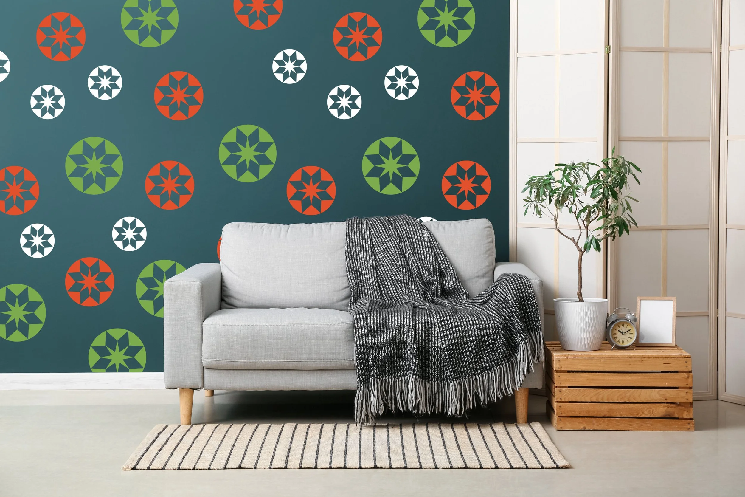Set of round geometric star quilt pattern wall decals in 3 sizes and 3 colors. Shown in white, orange, and lime green on a turquoise grey wall in a modern living room.