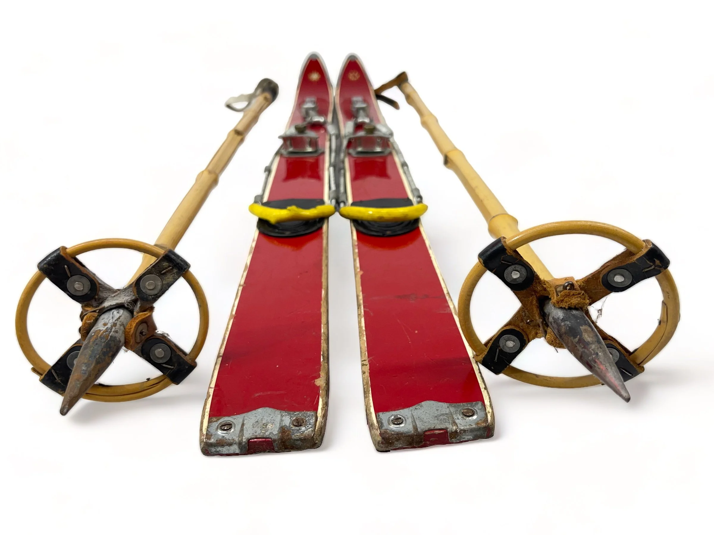 Pair of vintage red kids snow skis with metal bindings and bamboo ski poles, perfect for winter cabin or lodge decor.