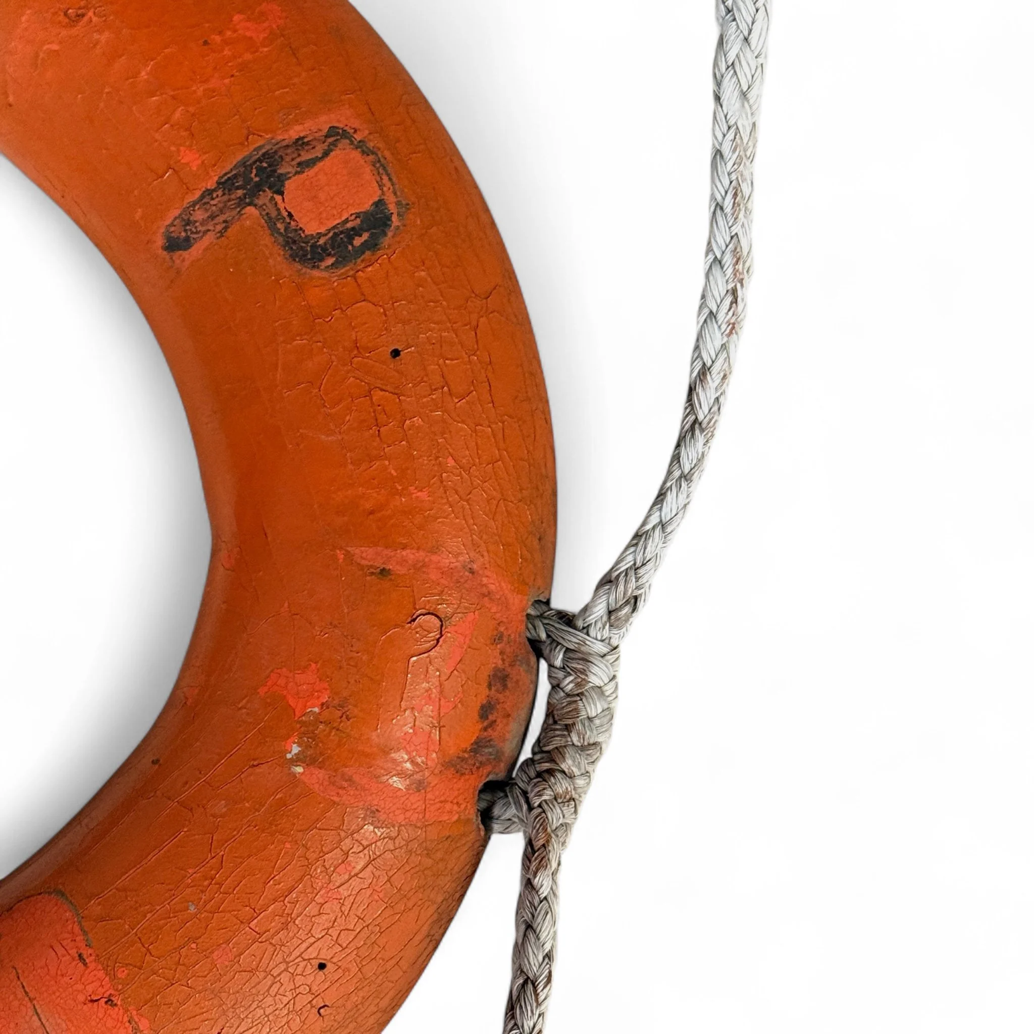 Close up view of a vintage life preserver with rope used as nautical wall decor, perfect for coastal, beach house, or maritime themed interior styling.