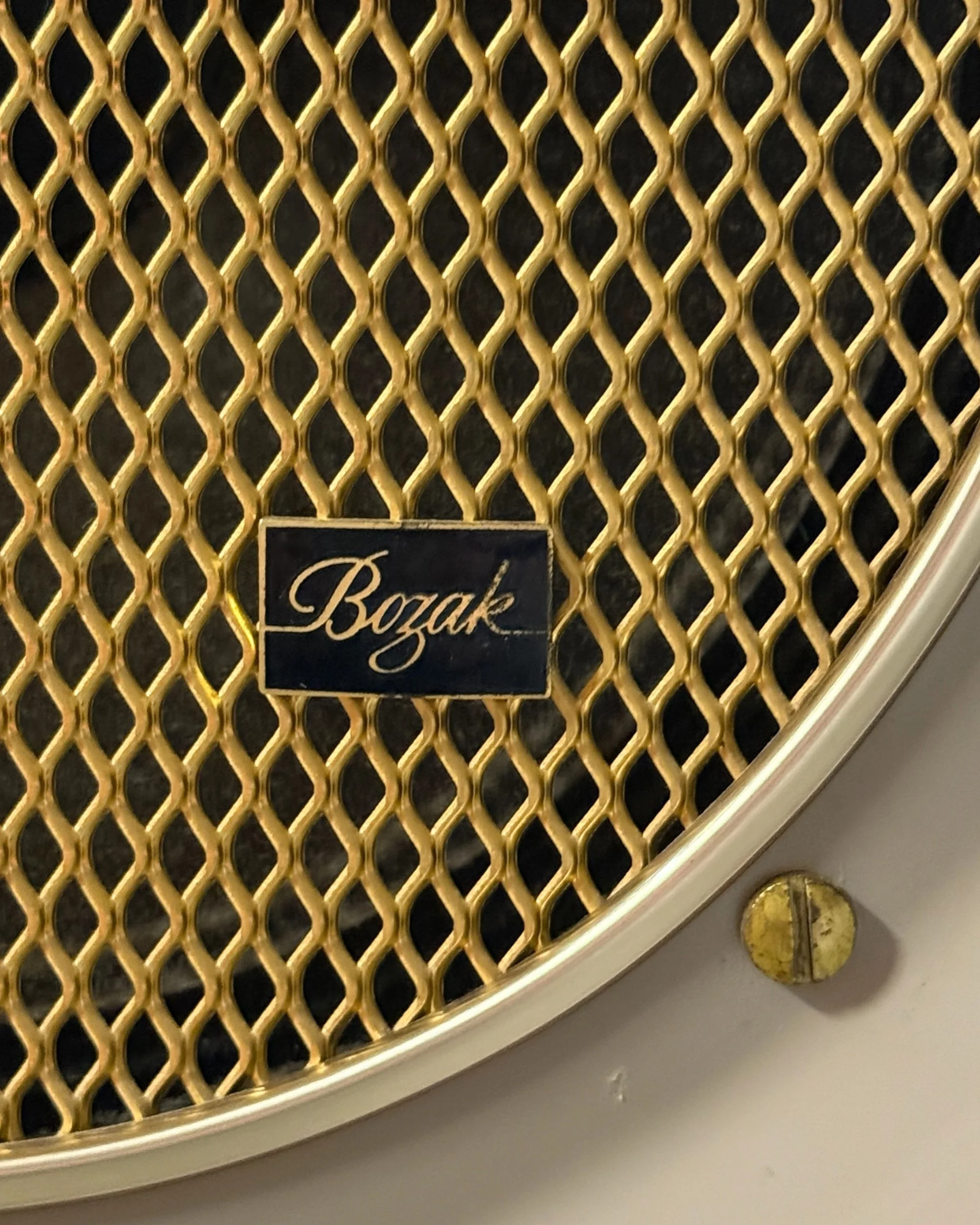 Close-up of the front of a circular vintage Bozak speaker, highlighting the golden mesh center grille and concave aluminum shell.
