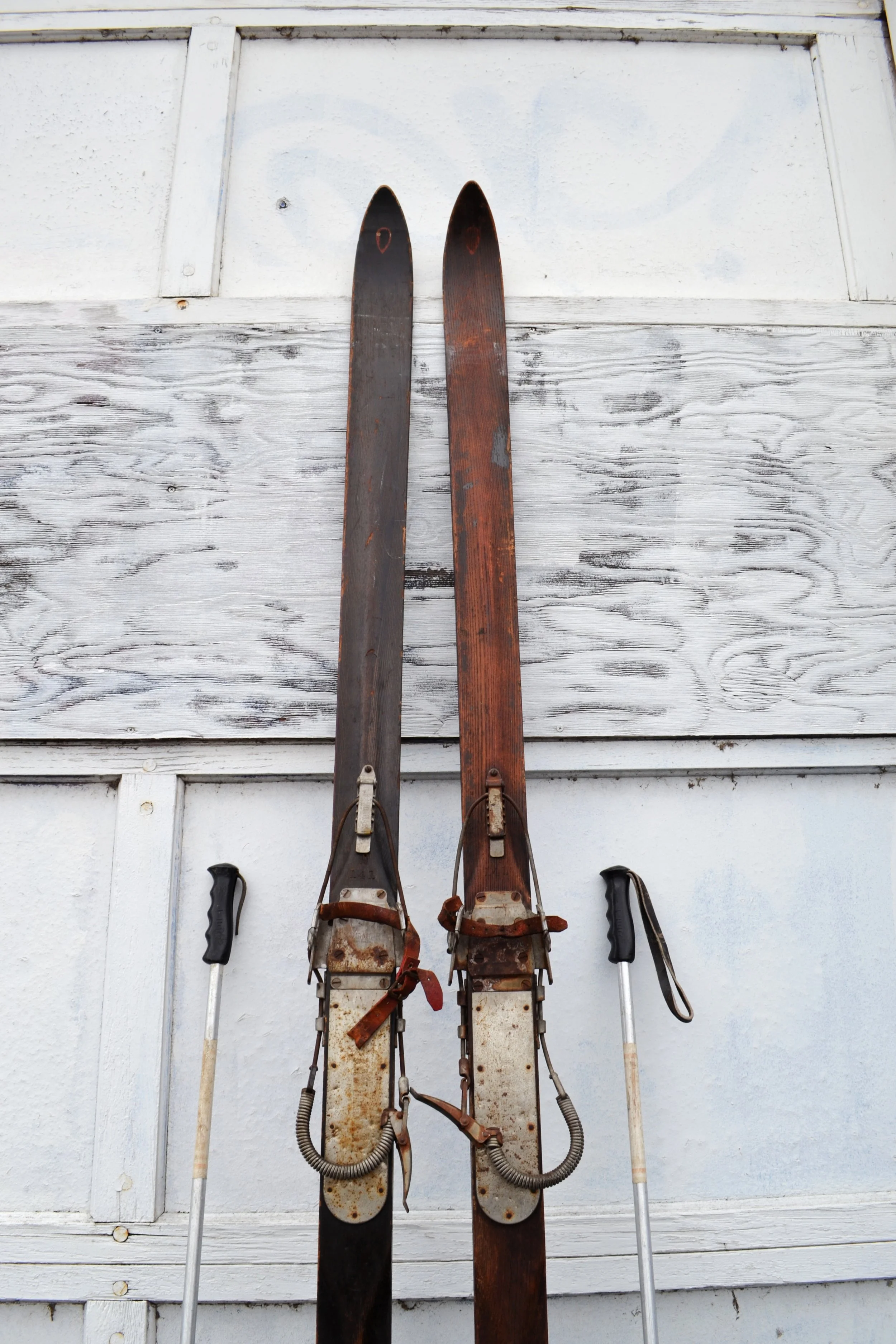 Vintage wooden snow skis with a dark finish and rustic metal bindings with vintage metal ski poles.