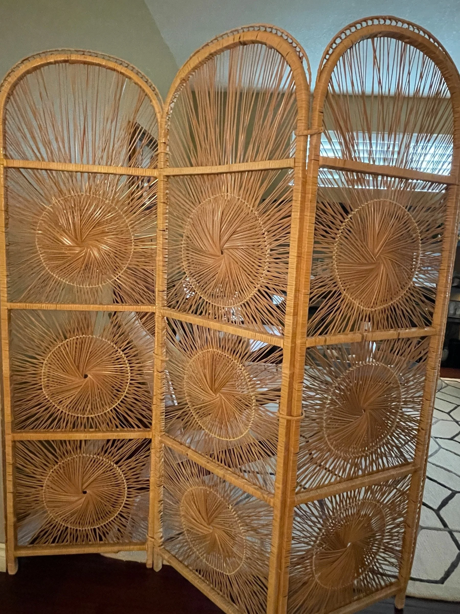 Vintage 1970s rattan room divider with sunburst pattern and rounded tops. Measures 71.5 inches tall displayed in a modern living room with potted plants and a mid century inspired chair.