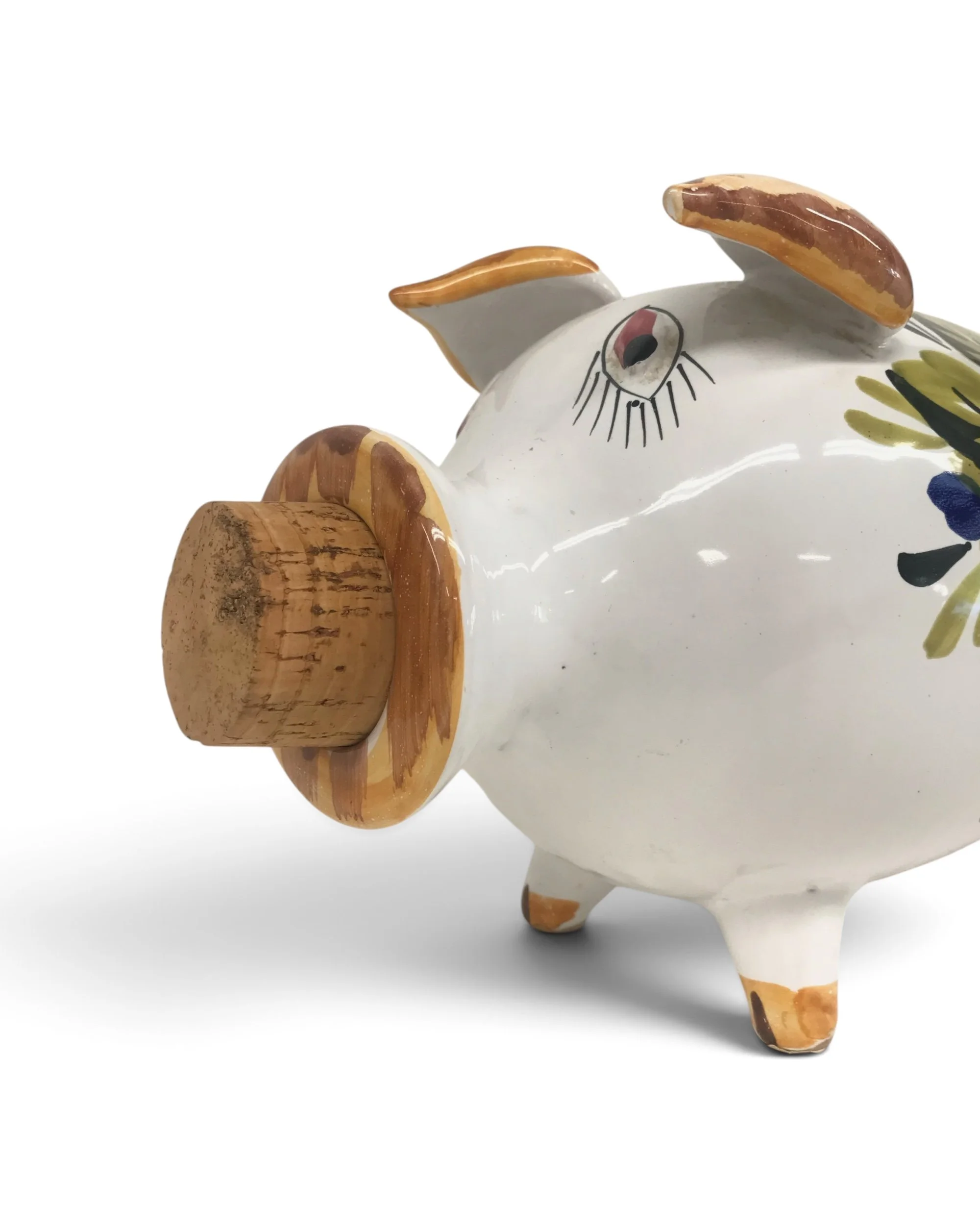 A white ceramic piggy bank featuring a brown cork stopper in the snout. The pig has hand-painted brown accents on the ears and feet, with a stylized eye and floral patterns in green and blue