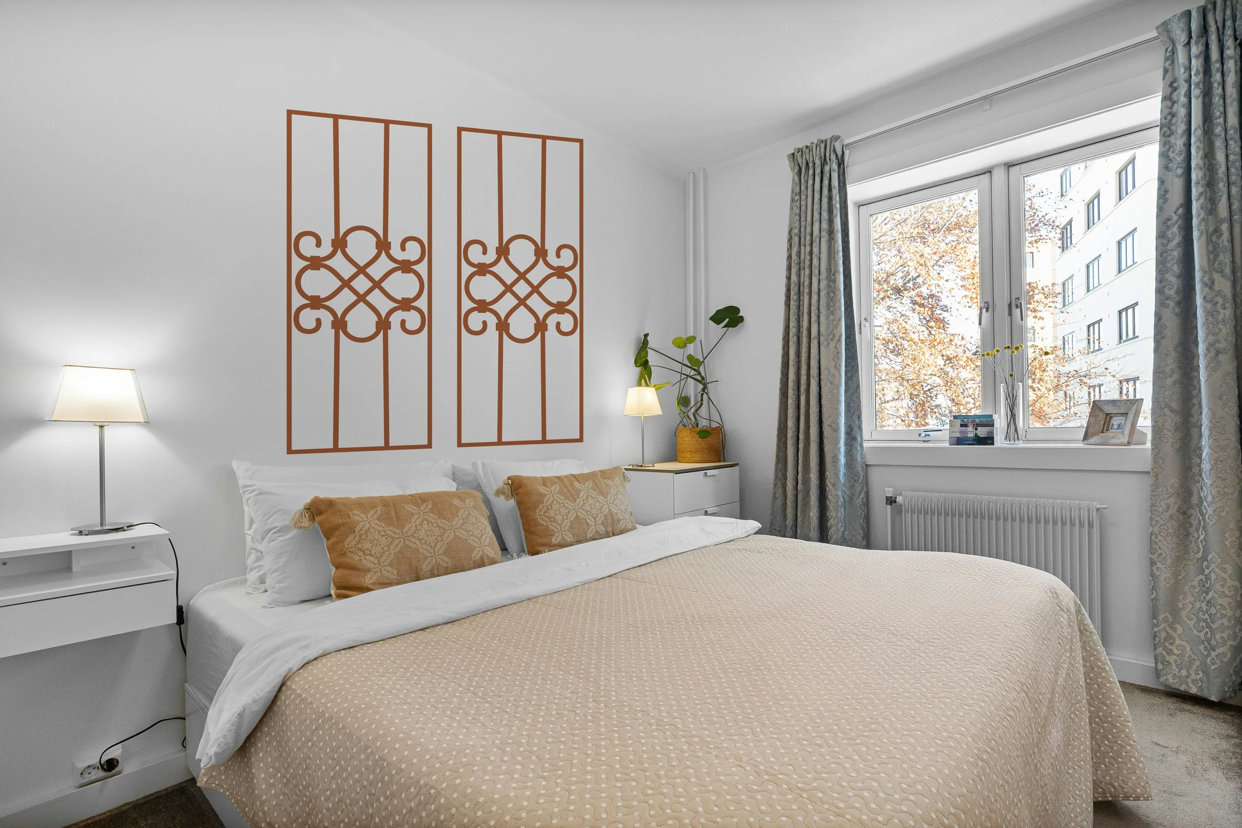 Pair of geometric scrollwork removable vinyl wall decals installed above a king bed in a bright minimalist bedroom.