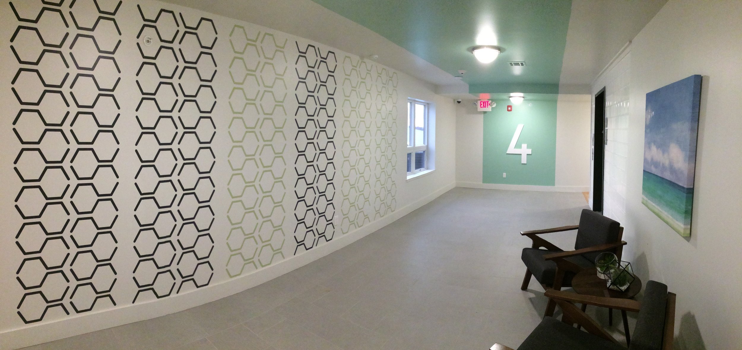 Hexagon geometric pattern wall decals shown in black and celedon on a white wall in the hallway on the 4th floor of an apartment complex.