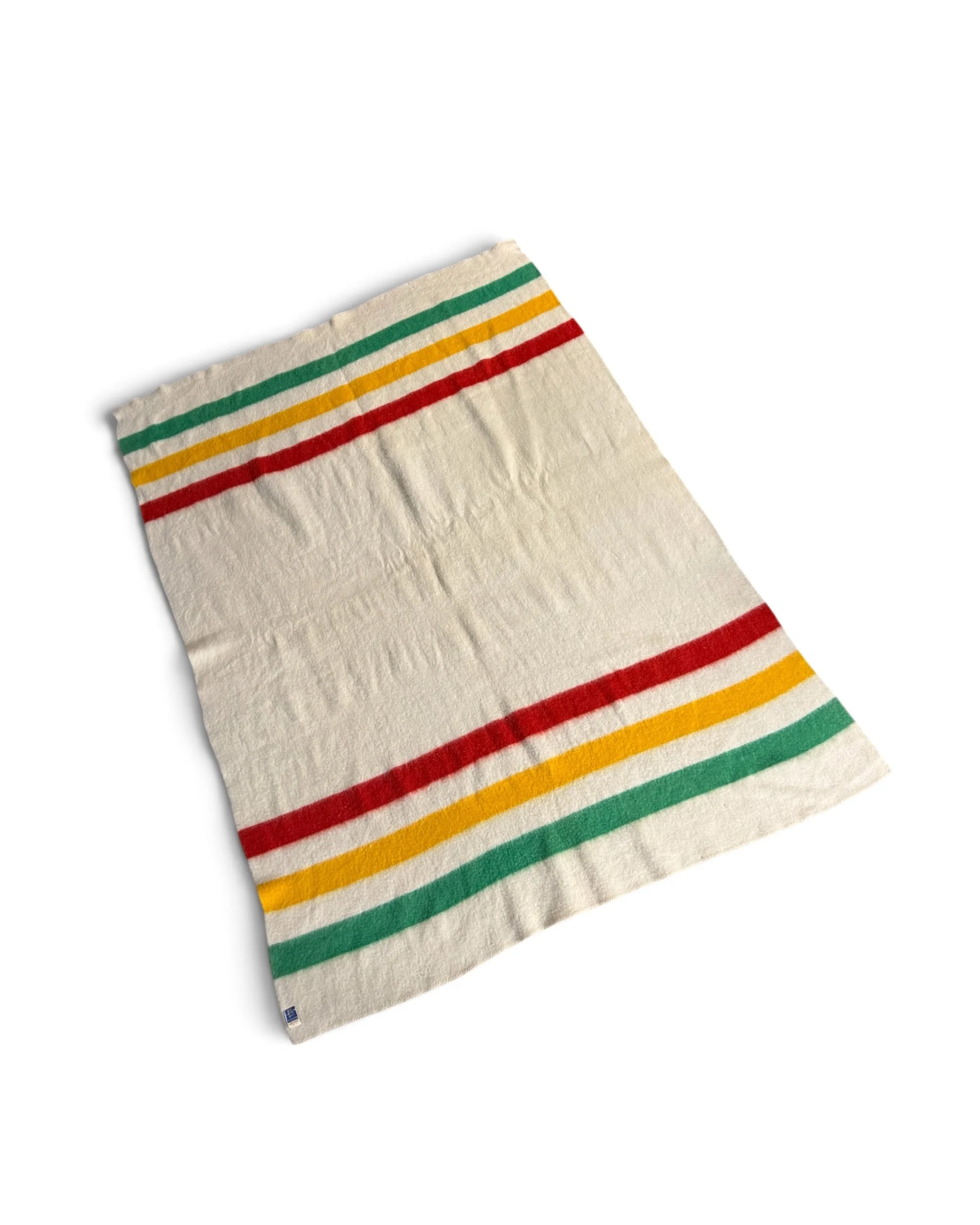 A 1950s vintage cream wool camp blanket with green, yellow, and red horizontal stripes laid flat, showcasing a rustic cabin style.