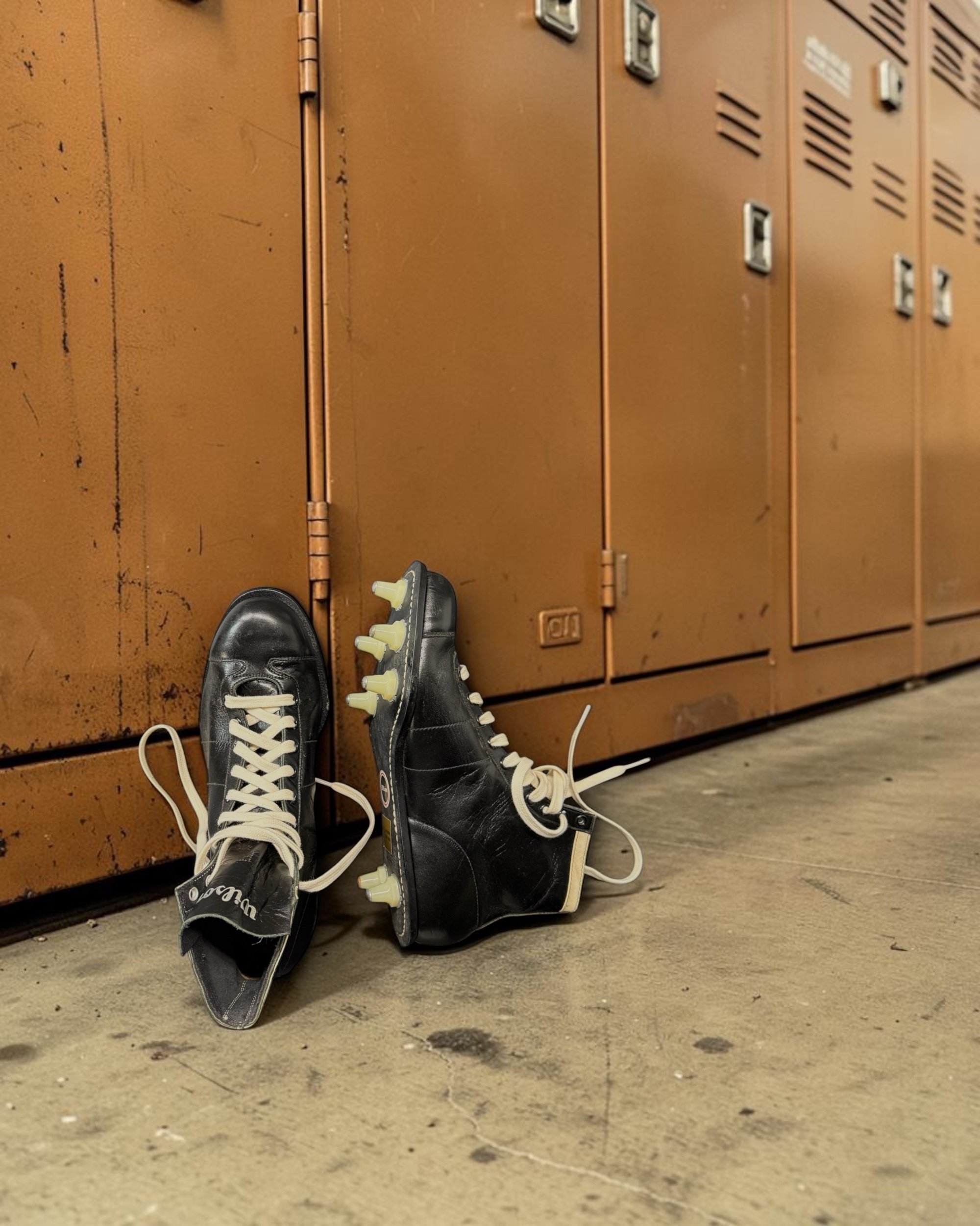 Pair of 1950s Wilson high-top football cleats in black leather, styled in an old school locker room.