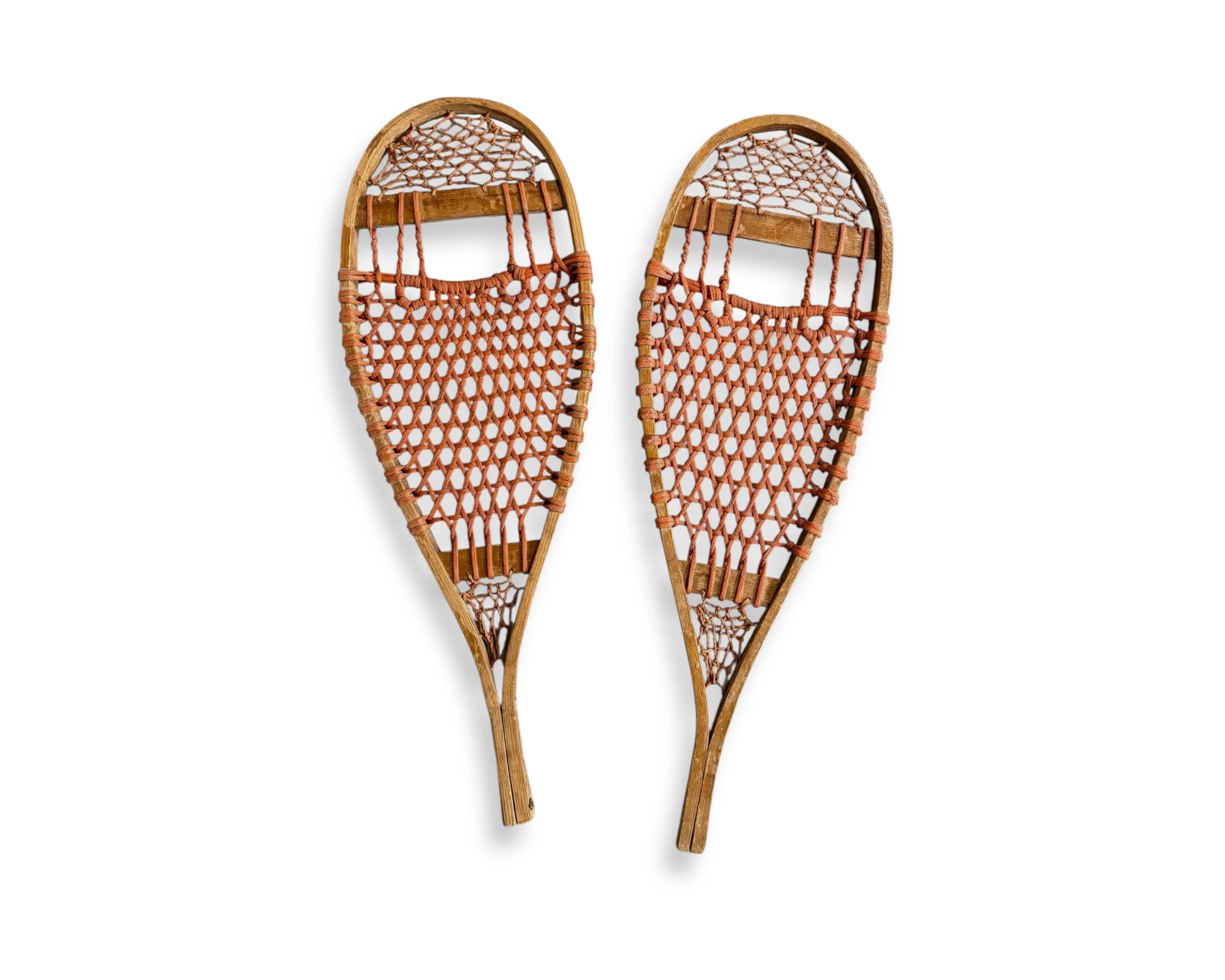 Pair of vintage wooden snowshoes with orange woven webbing on white background