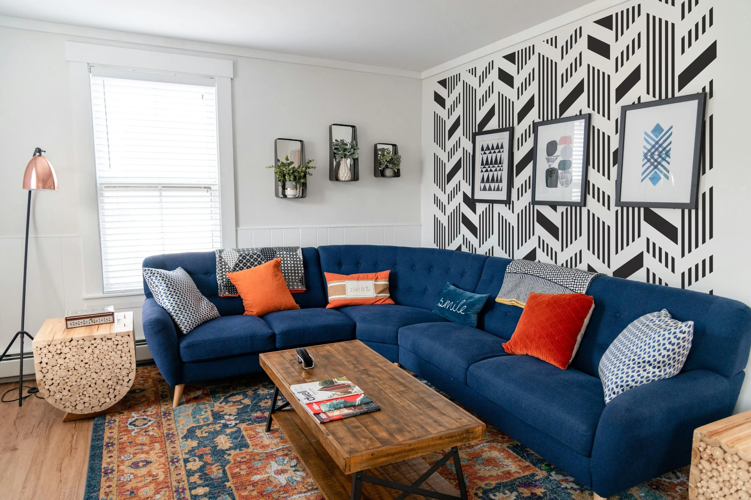 Renter-friendly peel-and-stick geometric wall decal paired with navy furniture, walnut coffee table, colorful vintage rug, and framed artwork.