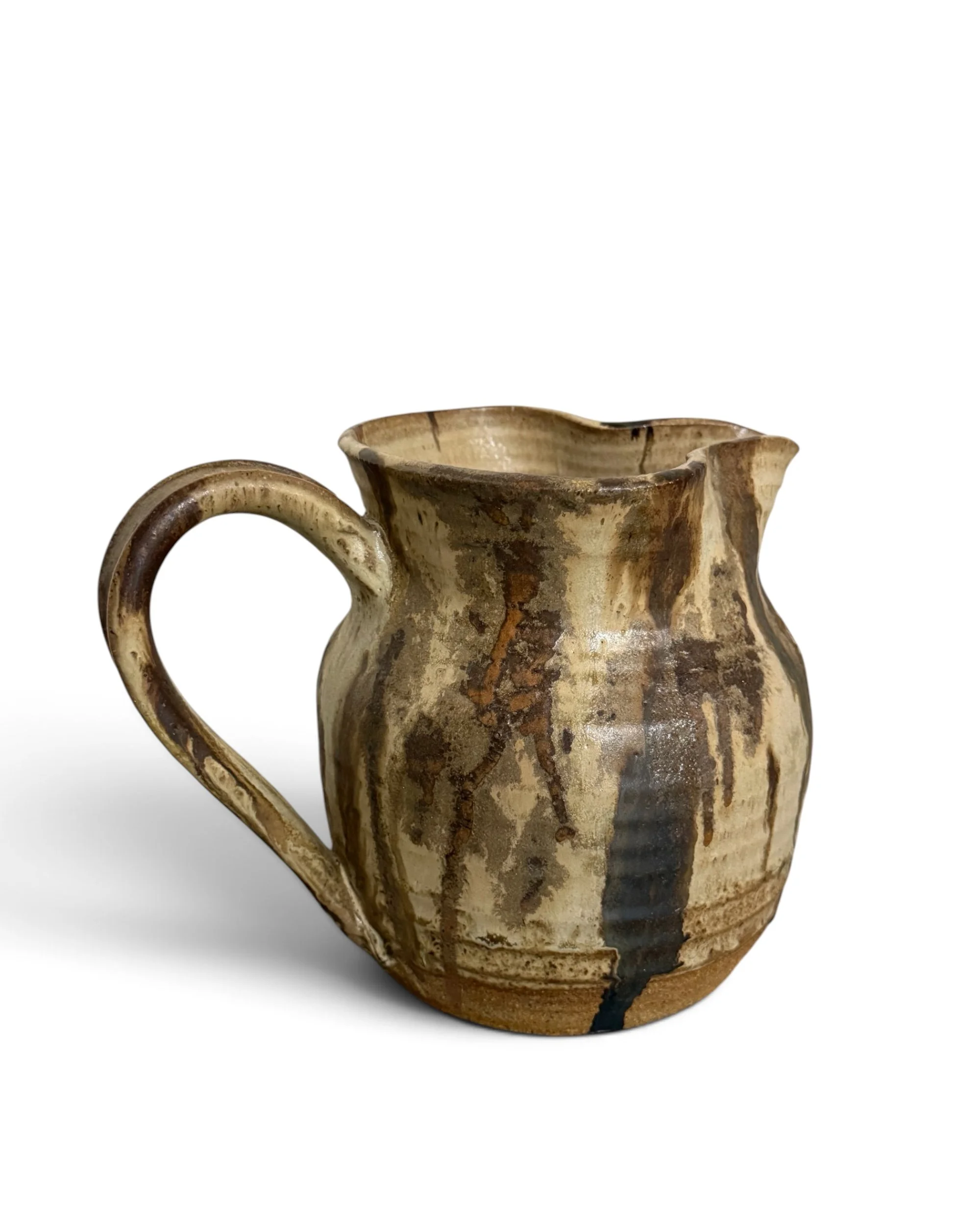 Side view of a vintage pottery pitcher showing its rounded ceramic form, handle, and rustic drip glaze finish.