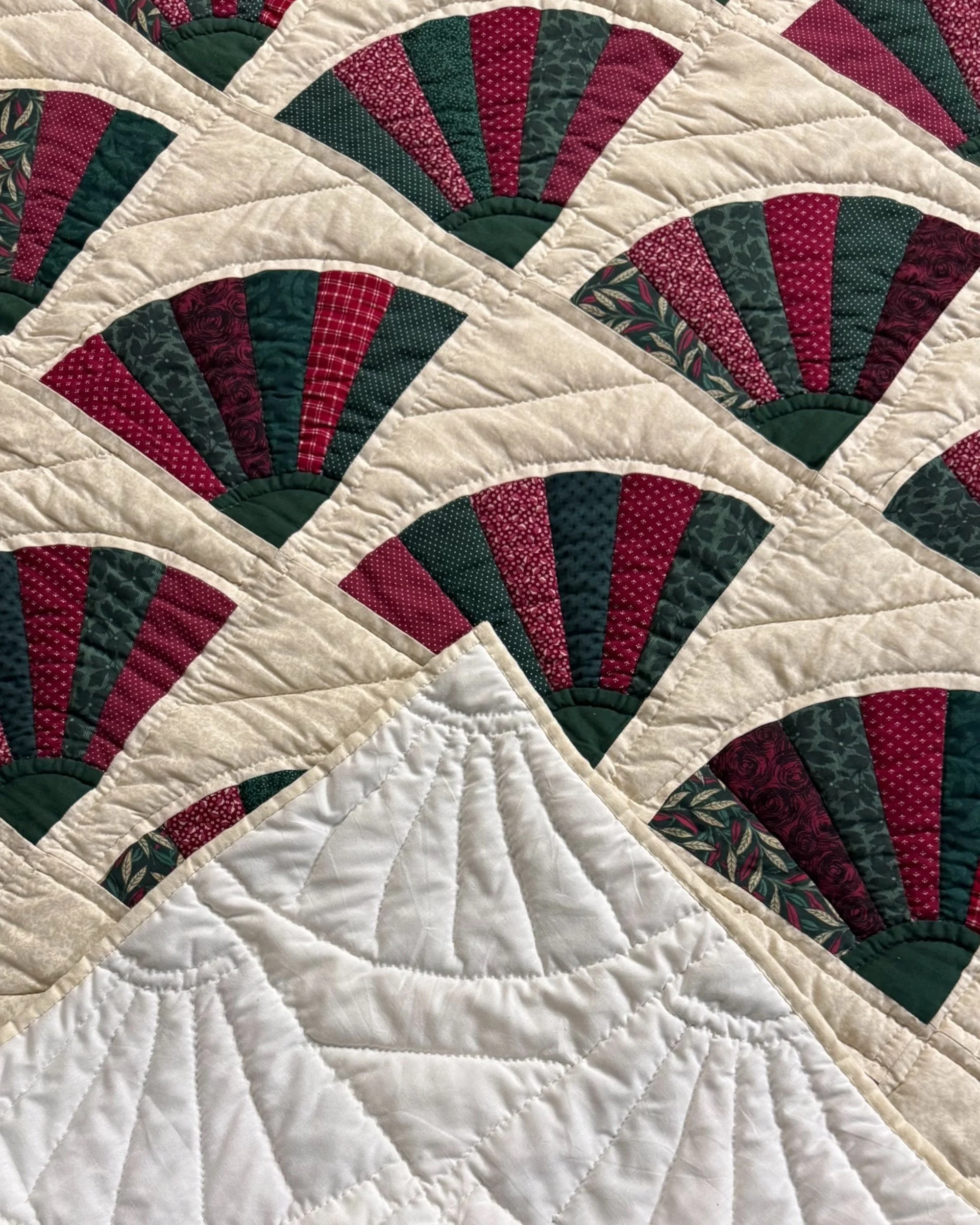 close up view of Grandmother's fan pattern on vintage handmade quilt in burgundy, forest green and light beige colors.
