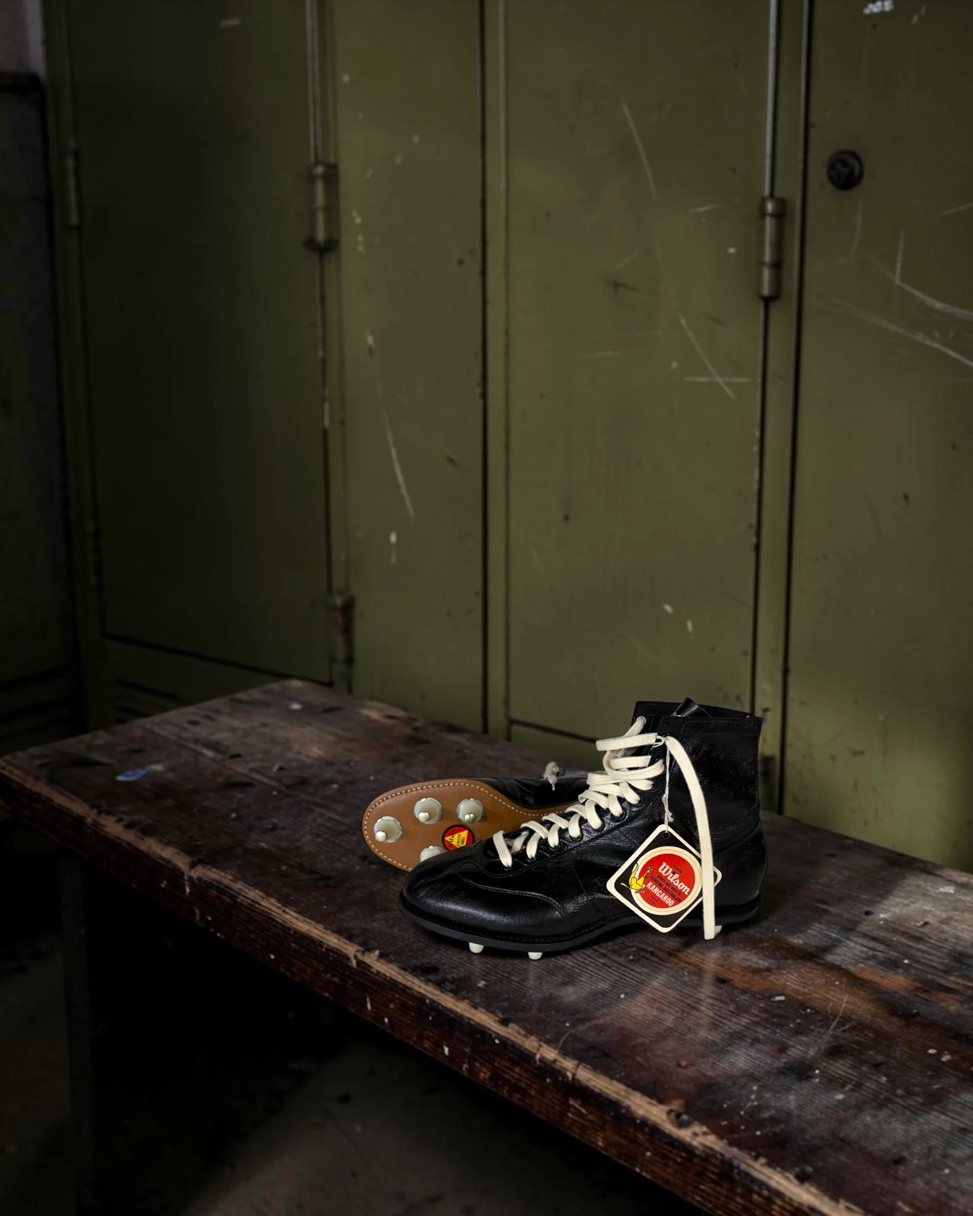 vintage 1950s NOS Wilson football cleats styled on a bench in an old school locker room as athletic decor.