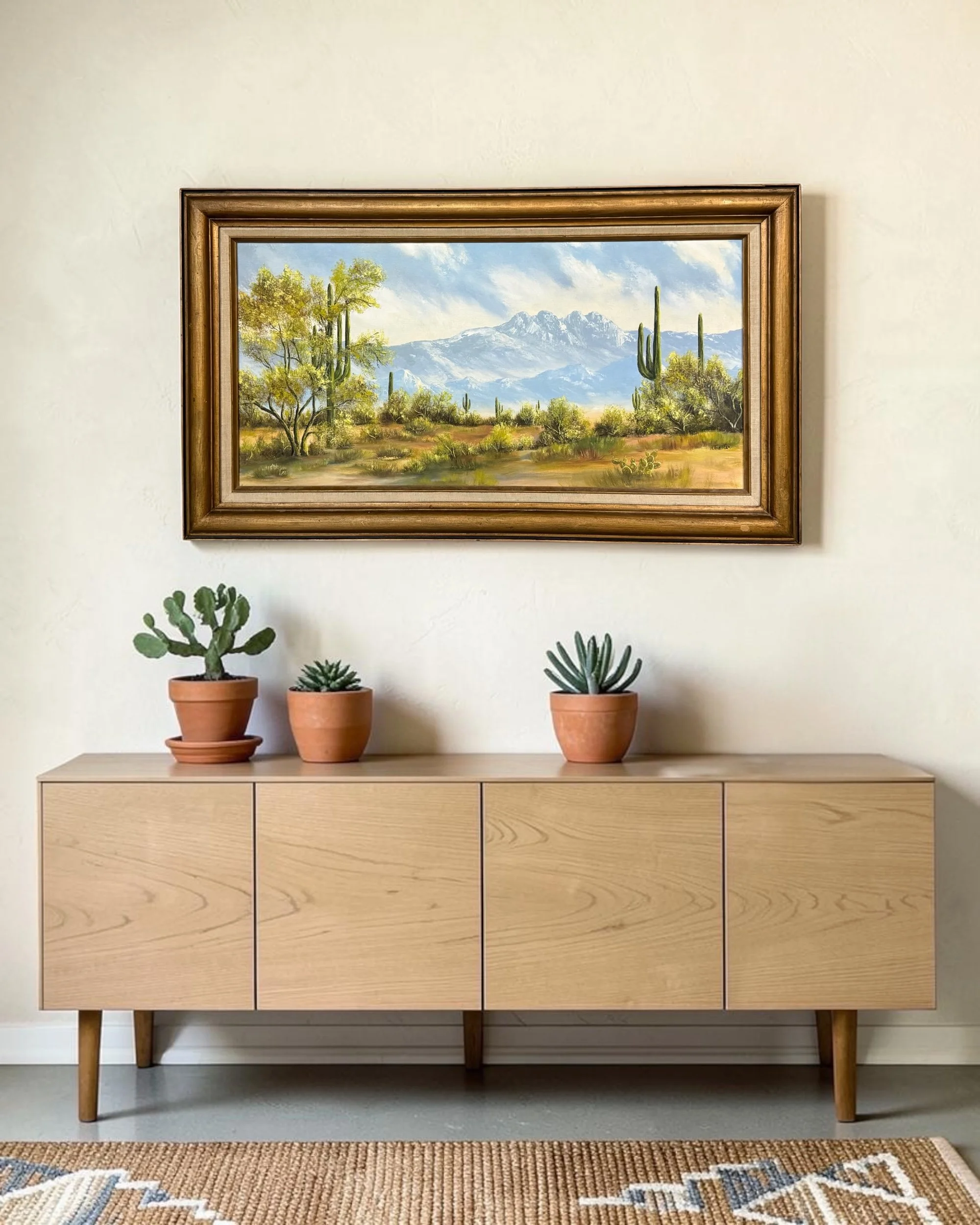 Framed Western landscape art depicting Sonoran Desert cacti and panoramic mountain views, shown displayed above a credenza in a modern southwestern interior.