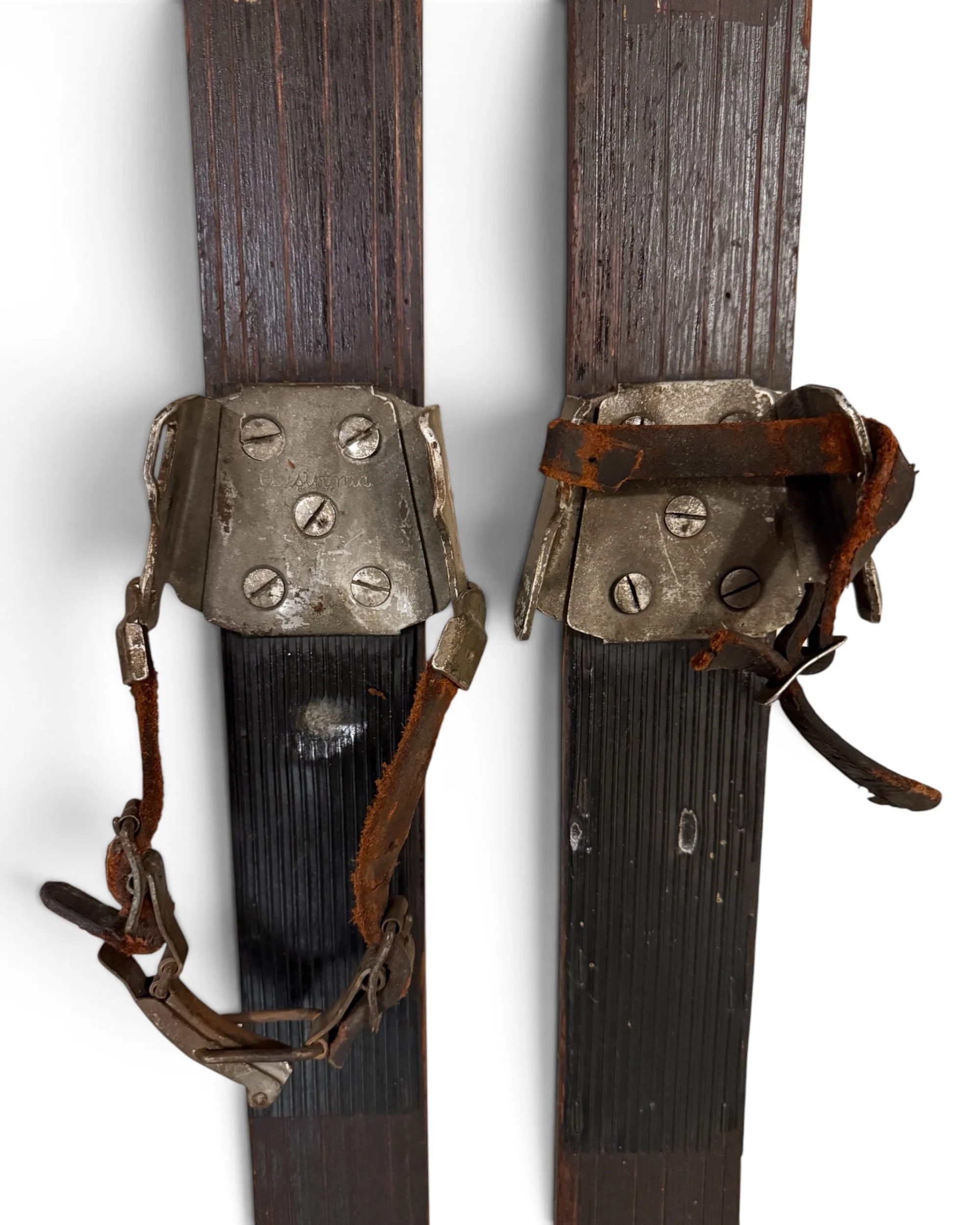 close up of vintage wooden snow skis with metal and leather bindings with the brand "Austronia" displayed on the metal.