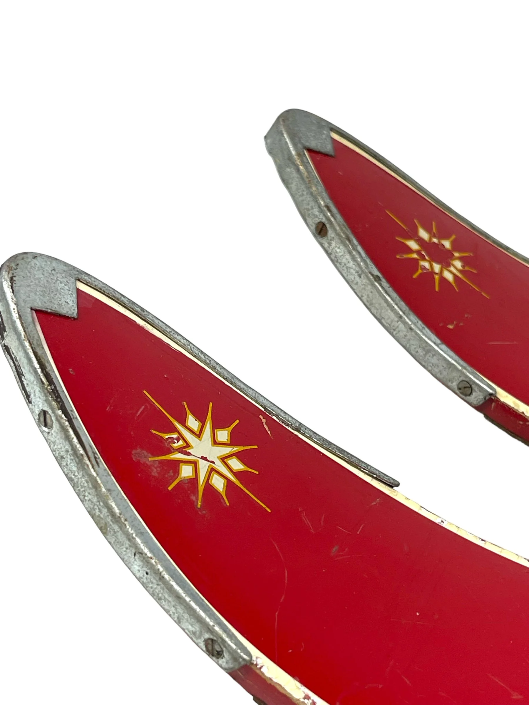 Close up view of tips on a pair of vintage red kids snow skis with metal bindings and bamboo ski poles, perfect for winter cabin or lodge decor.