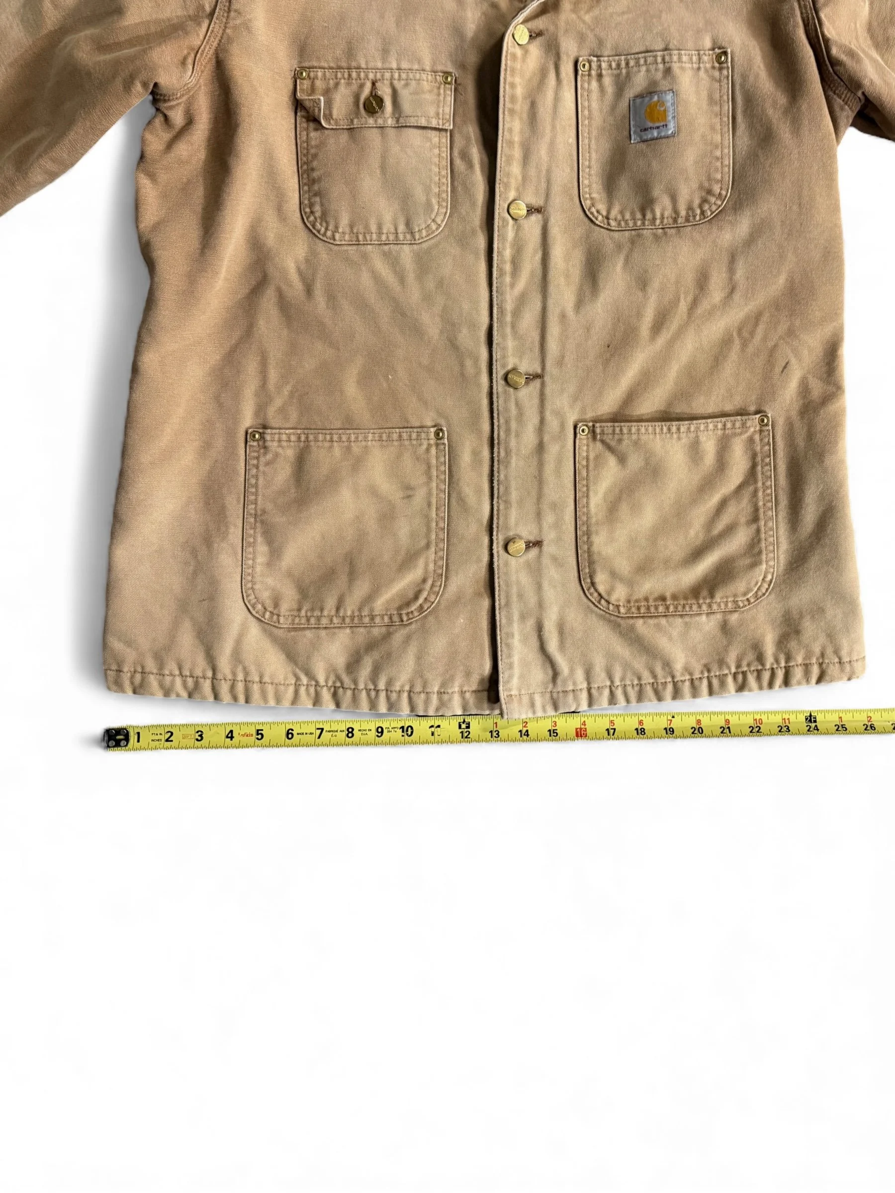 Close up view of bottom half of vintage Carhartt chore jacket with a ruler showing measurements