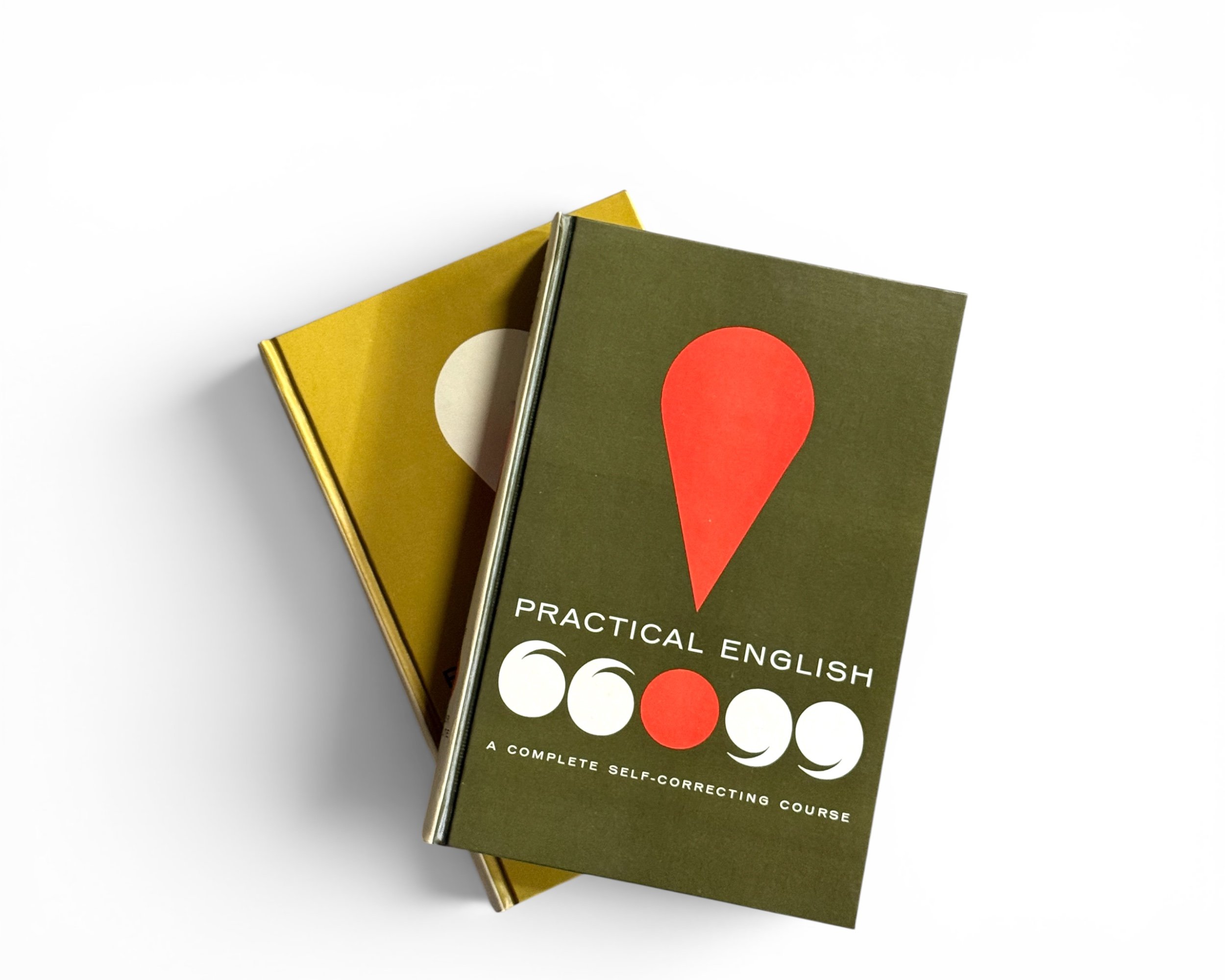 Top view of the stacked vintage book set highlighting the matte olive-green cover of Volume 2, showcasing its bold geometric red teardrop graphic and white quotation marks motif.