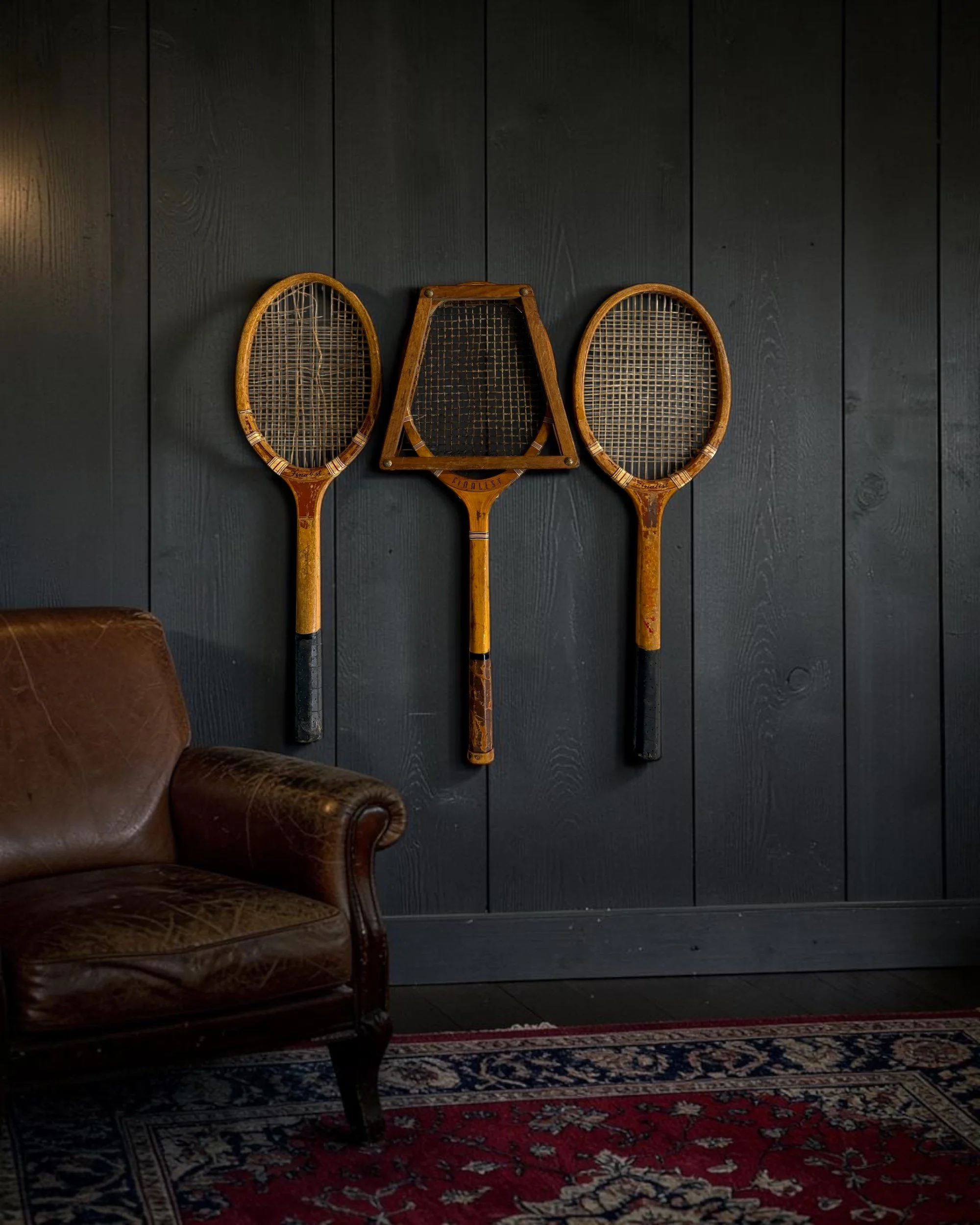 Vintage wooden tennis rackets styled as decorative wall art in a moody den.