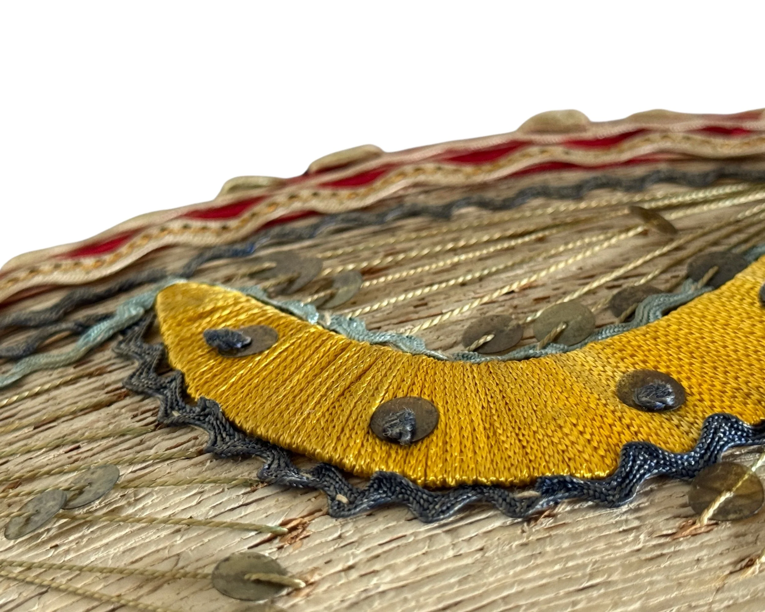 Close-up intricate details on a vintage sombrero. Featuring a yellow embroidered section with dark blue trim and sequins. The top edge has red and cream-colored ribbon.
