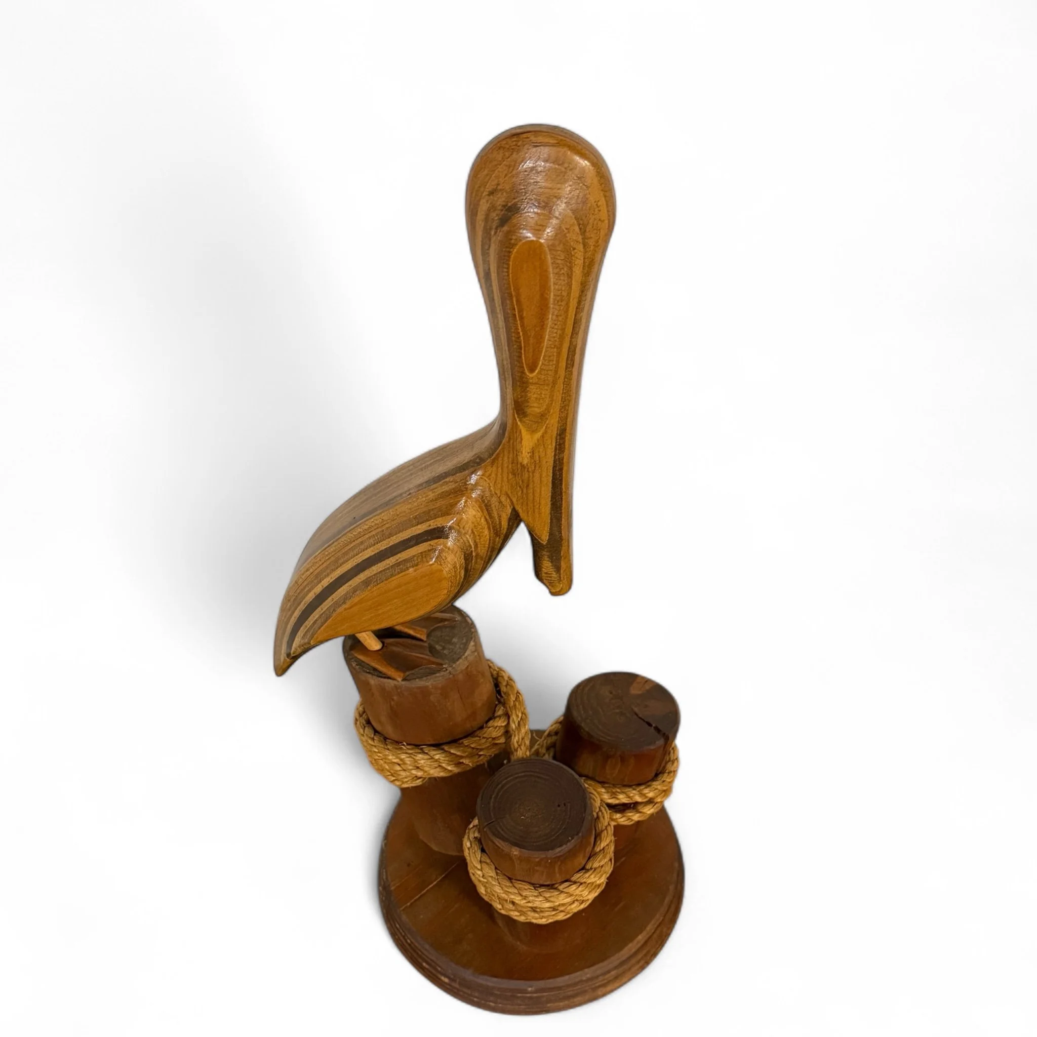 top view of vintage wooden carved pelican perched on a collection of 3 logs with ropes for seaside interiors.