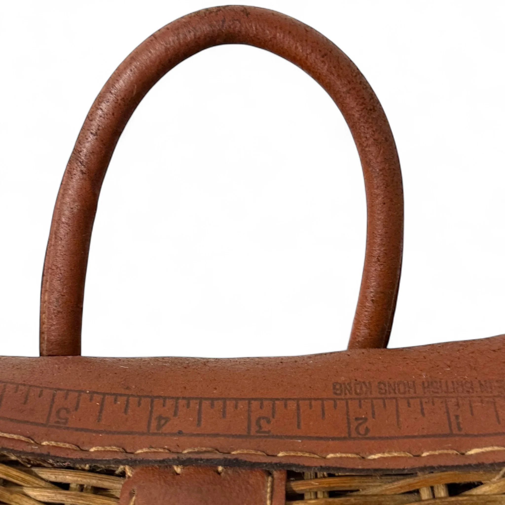 Close-up of handle and ruler on a vintage woven wicker creel basket with leather strap detail