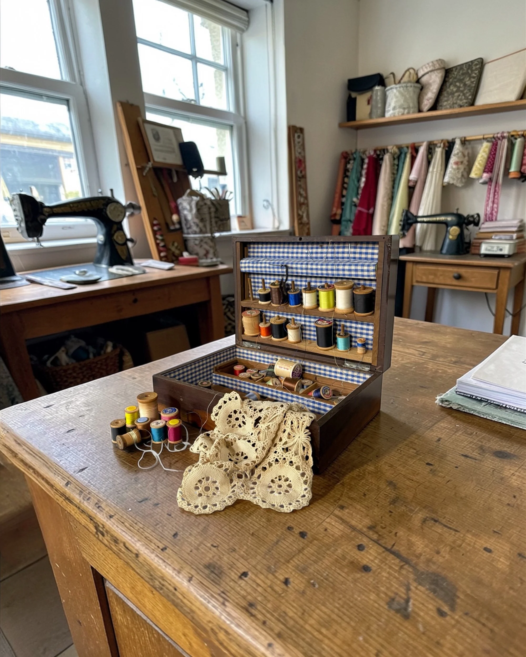 Vintage craft storage box with lace textile and sewing notions styled on a rustic wooden table in a sewing room.