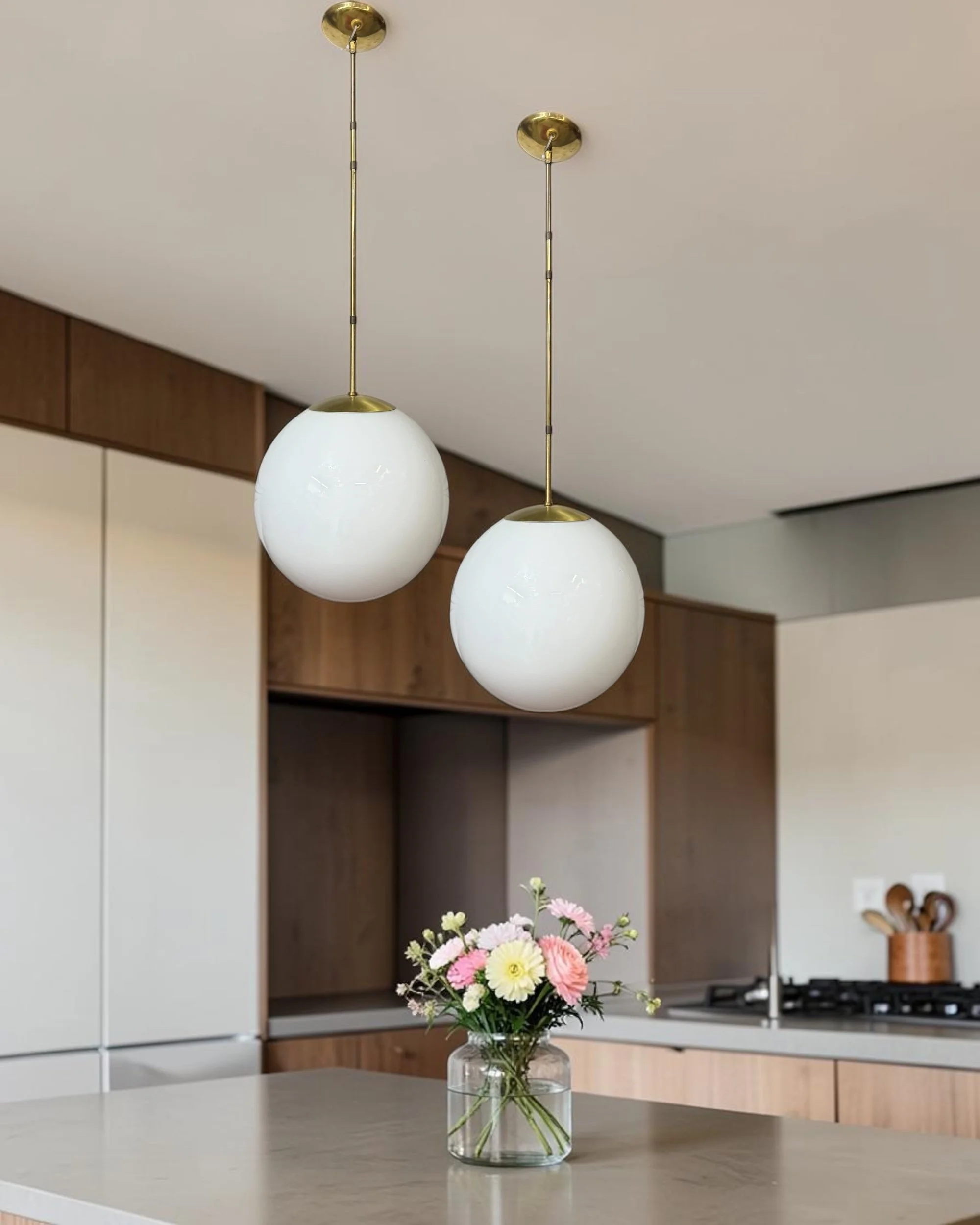Mid century modern hanging orb lights with brass downrod and white glass globe shown styled in a modern kitchen.