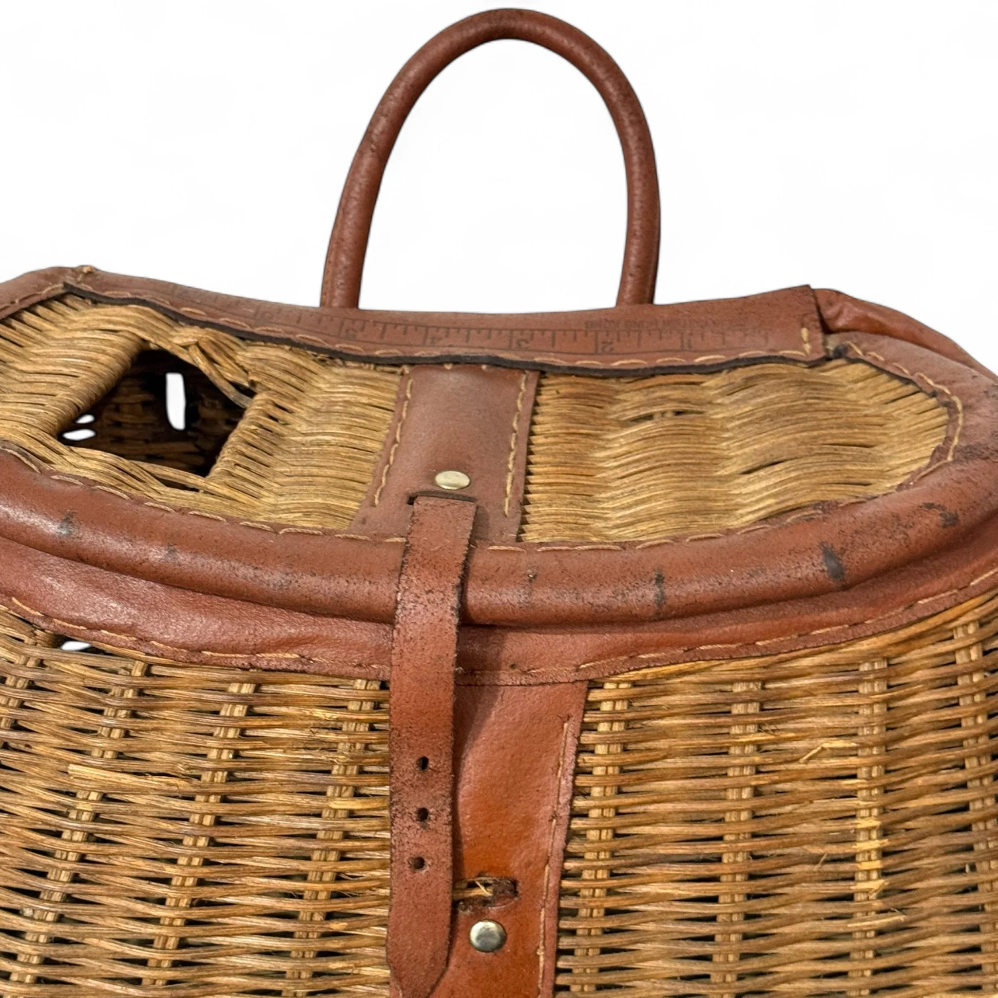 Close up detailed view of a vintage fishing creel basket made in British Hong Kong made of wicker and leather for rustic cabin or lodge decor.