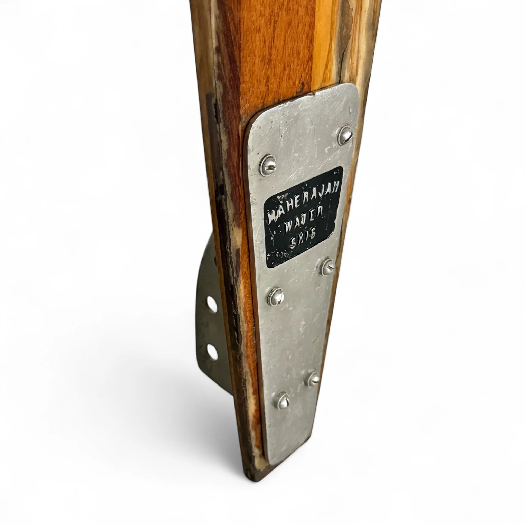 A close up view of the metal label on a 68 inch vintage wooden slalom water ski by Maherajah. The ski is made of hardwood and includes original bindings.