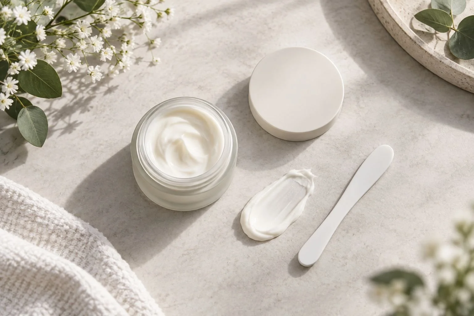 Unbranded cosmetic packaging beside a cream texture sample and a clean spatula