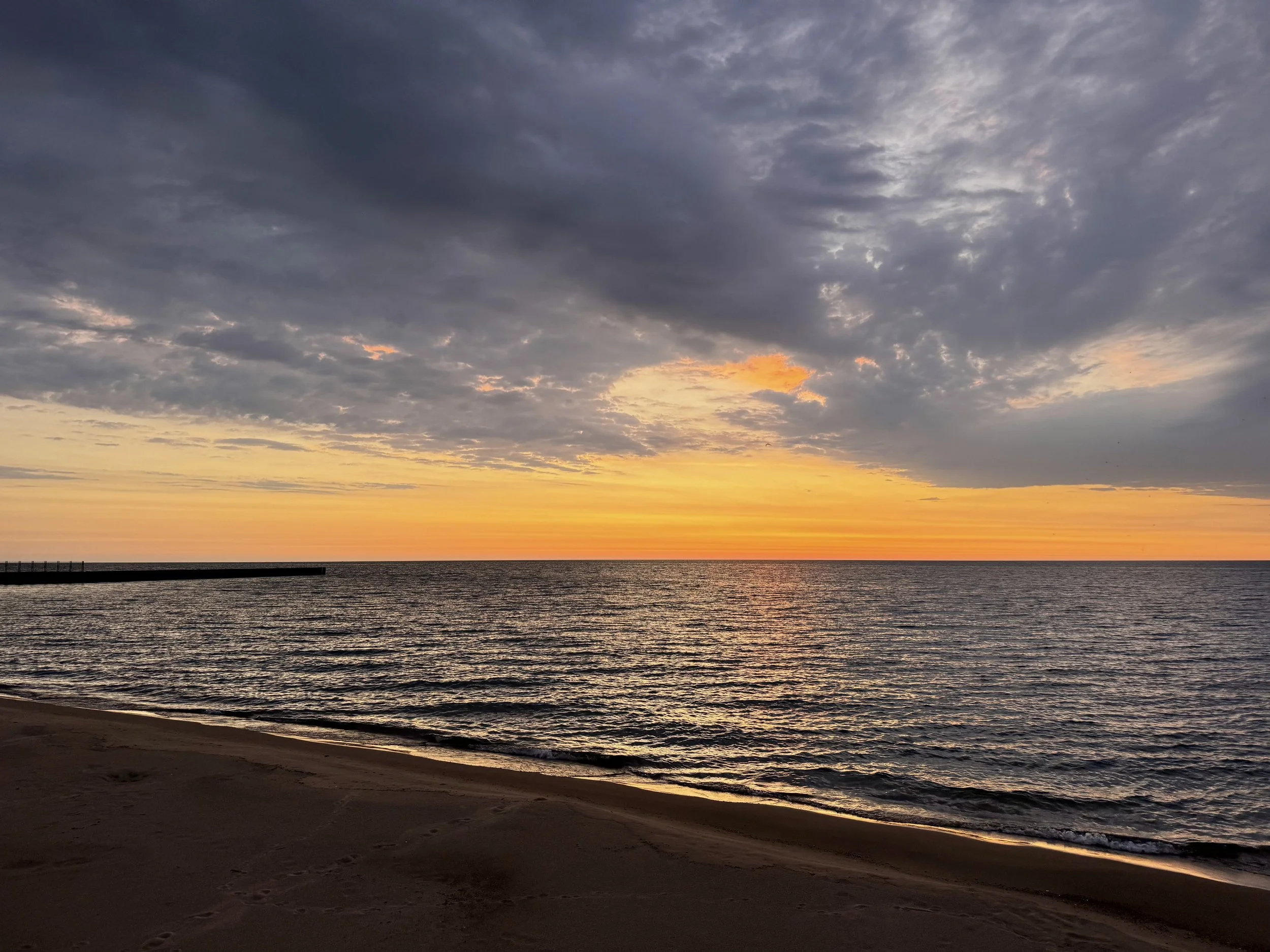 Sunset over Lake Michigan with a cloudy sky and a sandy beach in the foreground. Lee Street Beach, Evanston