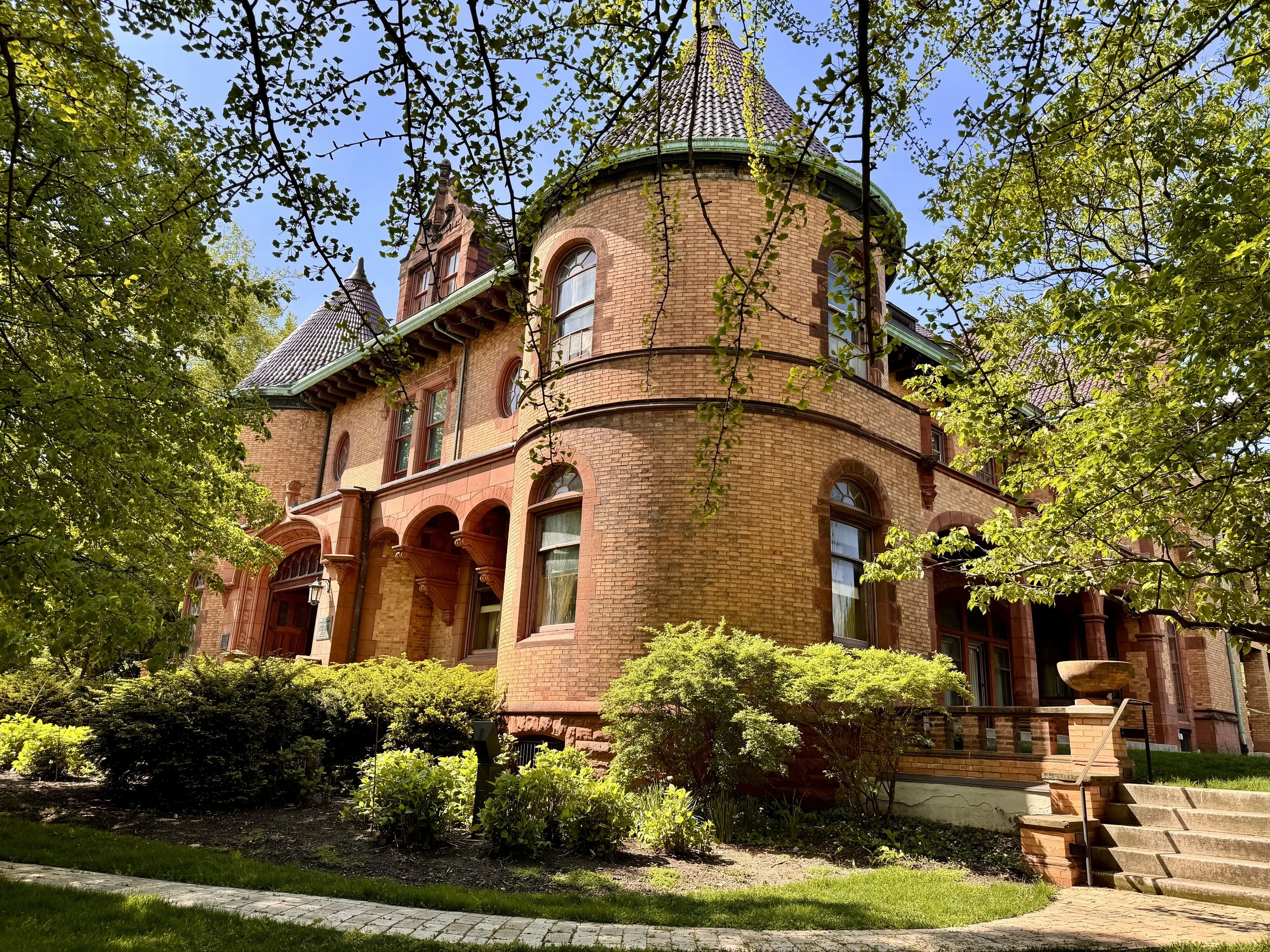 Home of Charles G. Dawes, former Vice President of the United States. A large, historic brick house with turreted towers, surrounded by trees and greenery, under a clear blue sky.
