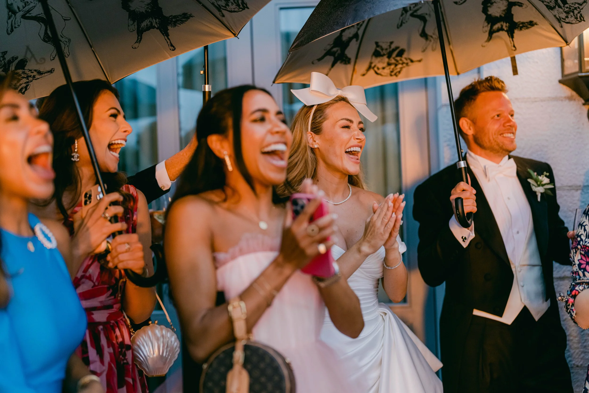 People smiling and enjoying a celebration under umbrellas outside during evening