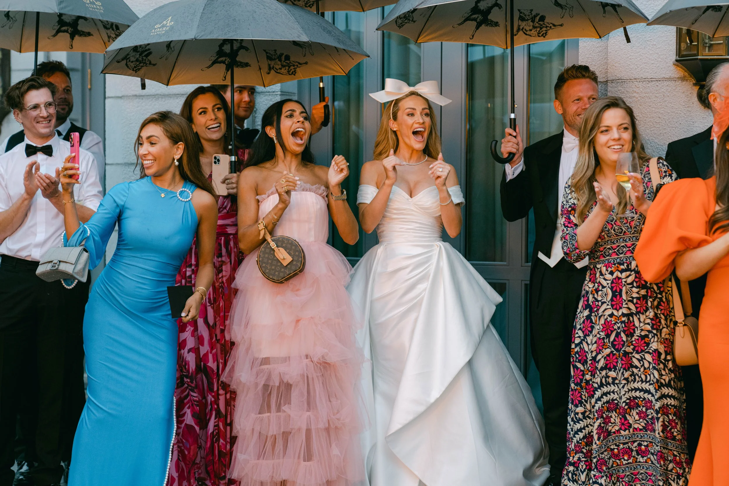 Group of people at a wedding celebration holding umbrellas, smiling, and taking photos.