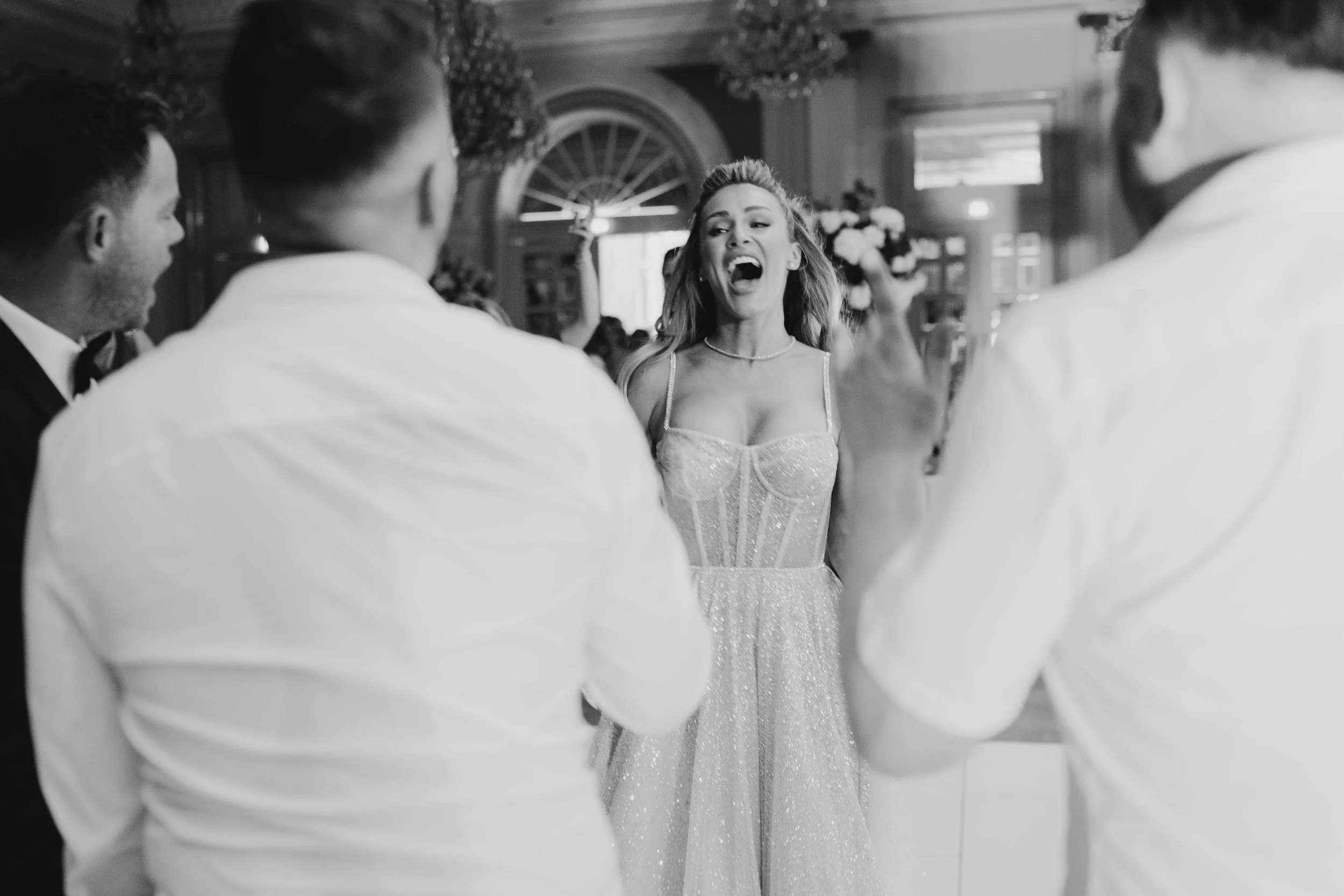 A woman in a sparkly dress joyfully celebrating with three men in formal attire at a wedding reception.