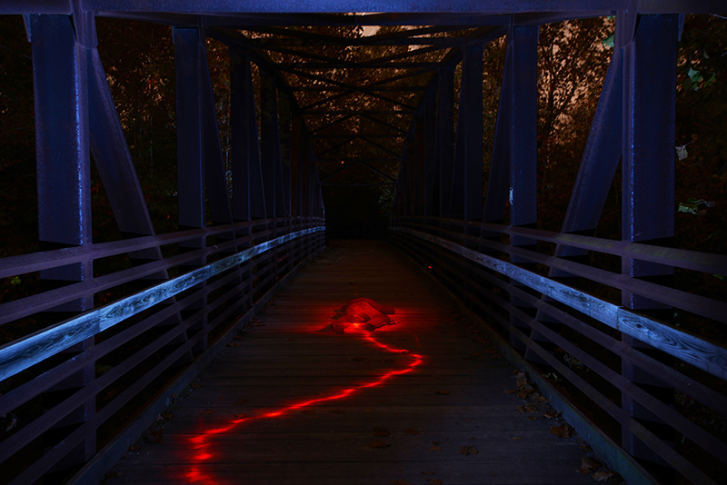 Matt McCormack lies in the middle of a bridge at Capen Park Tuesday evening October 21, 2014. The bridge is lit up using pops of an off-camera flash using a blue gel. Matt is lit with a flash light with a red gel. 
