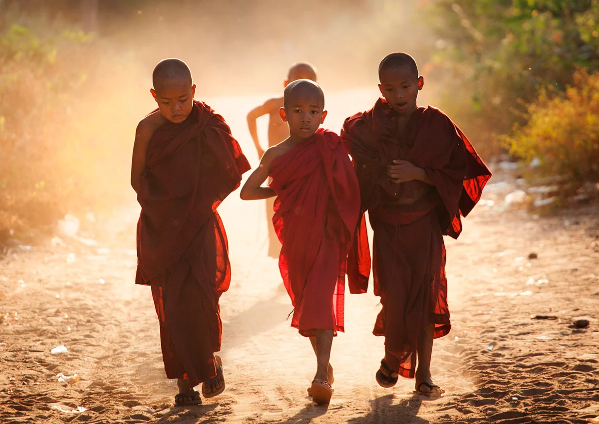 monks walk up a dirt track in a small village