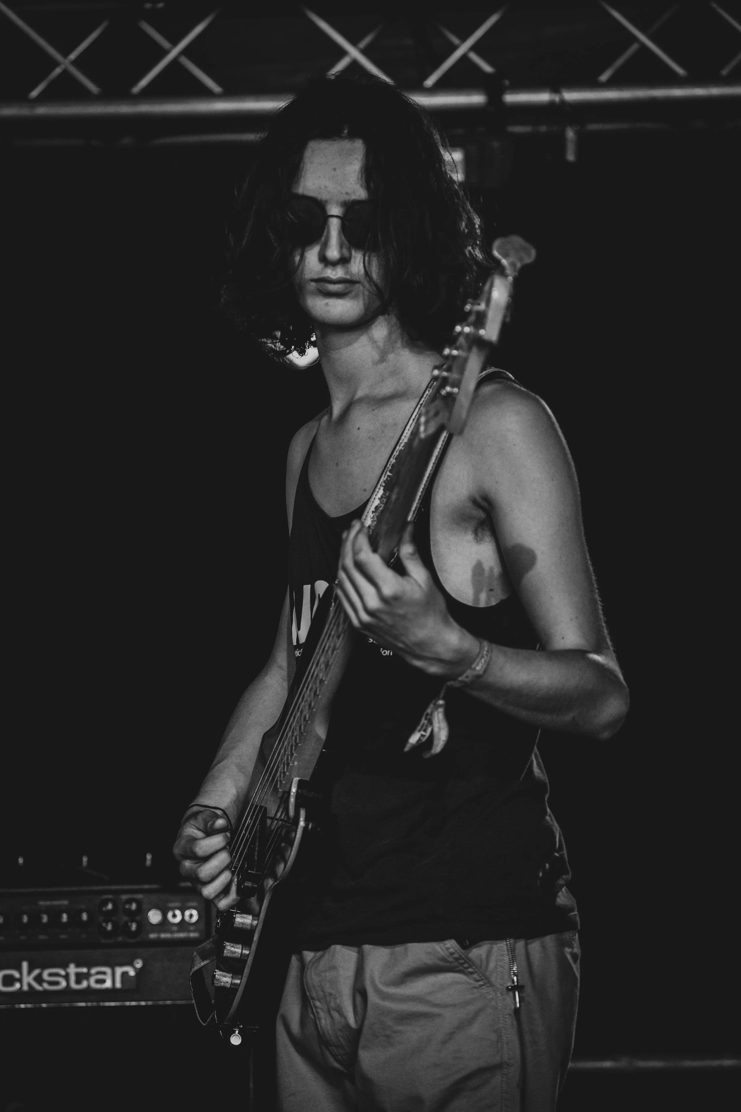 A woman playing an electric guitar on stage, wearing sunglasses and casual clothing, in a black and white photograph.
