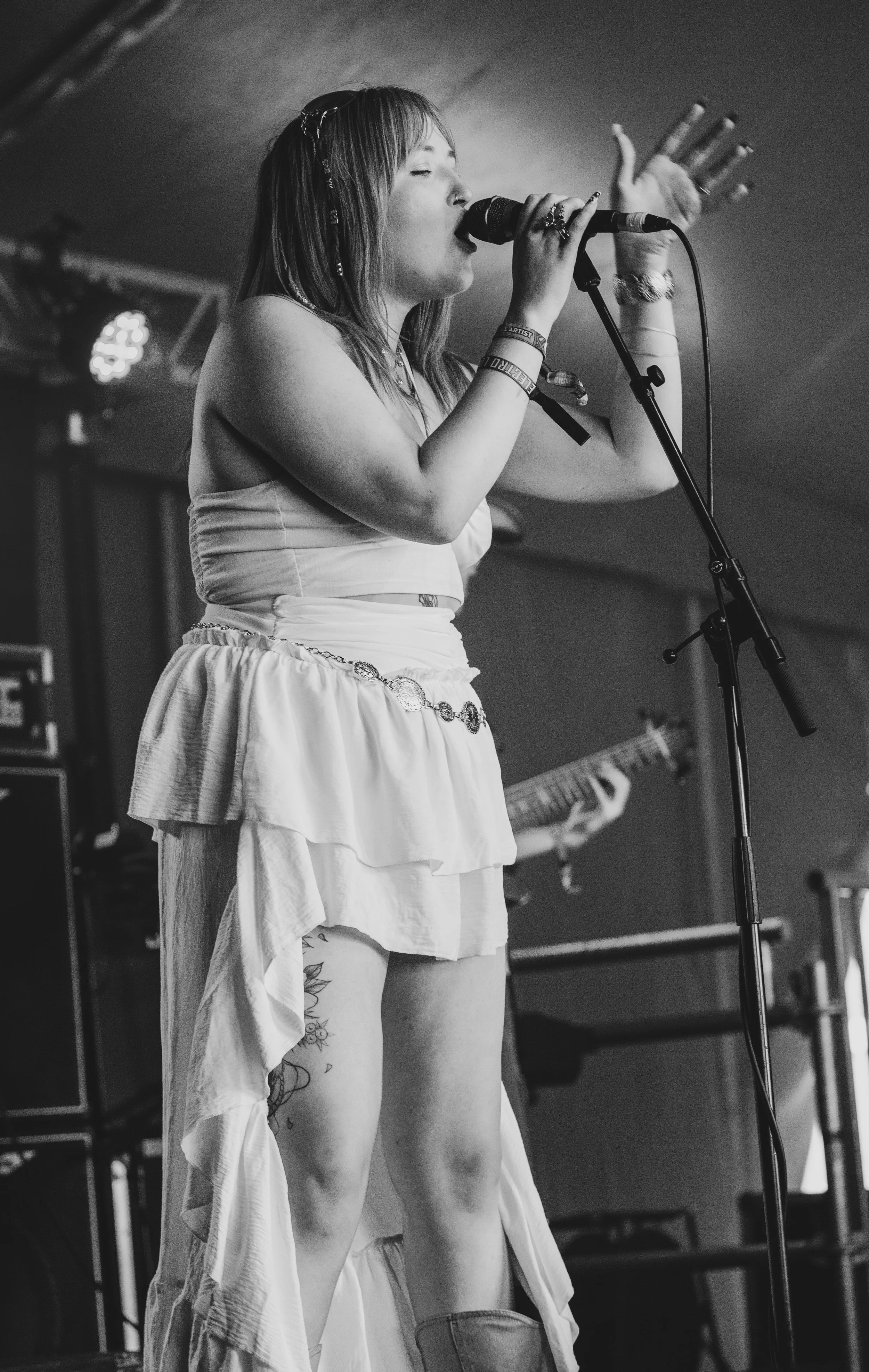 Georgia Nicole playing the Platform one stage at the Isle of Wight festival singing on stage, wearing a strapless top and layered skirt with jewellery, with a drummer in the background and stage lights overhead.
