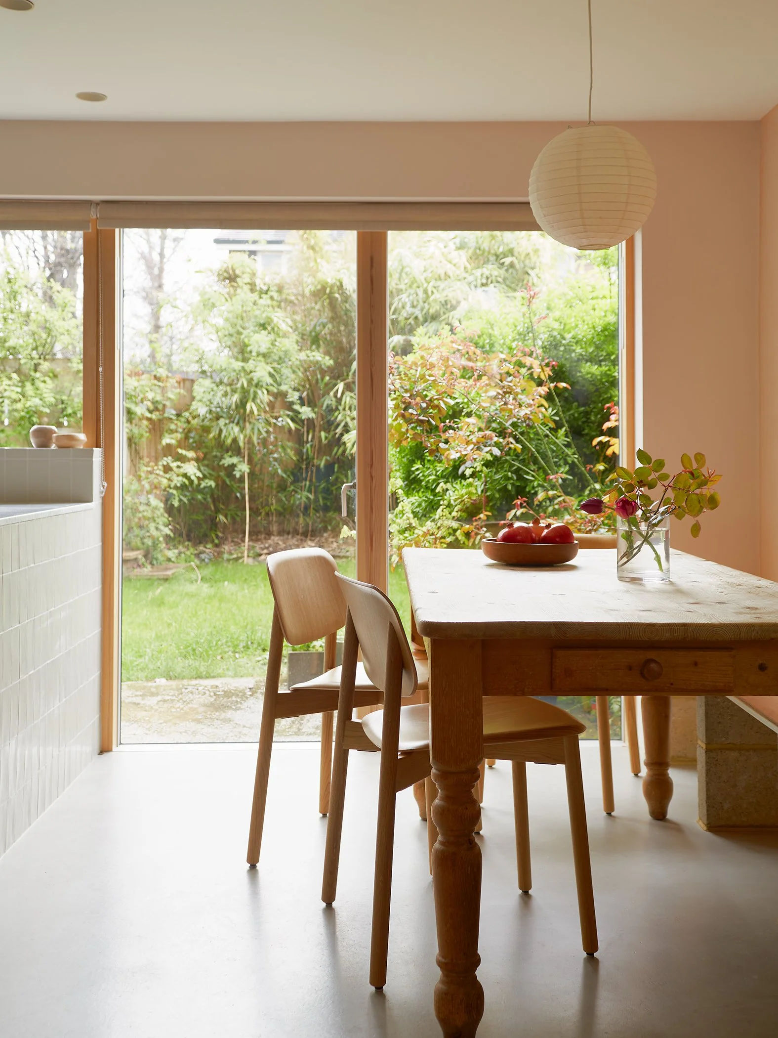 Bright dining room with wooden table, chairs, and a large window/view of a green garden outside.