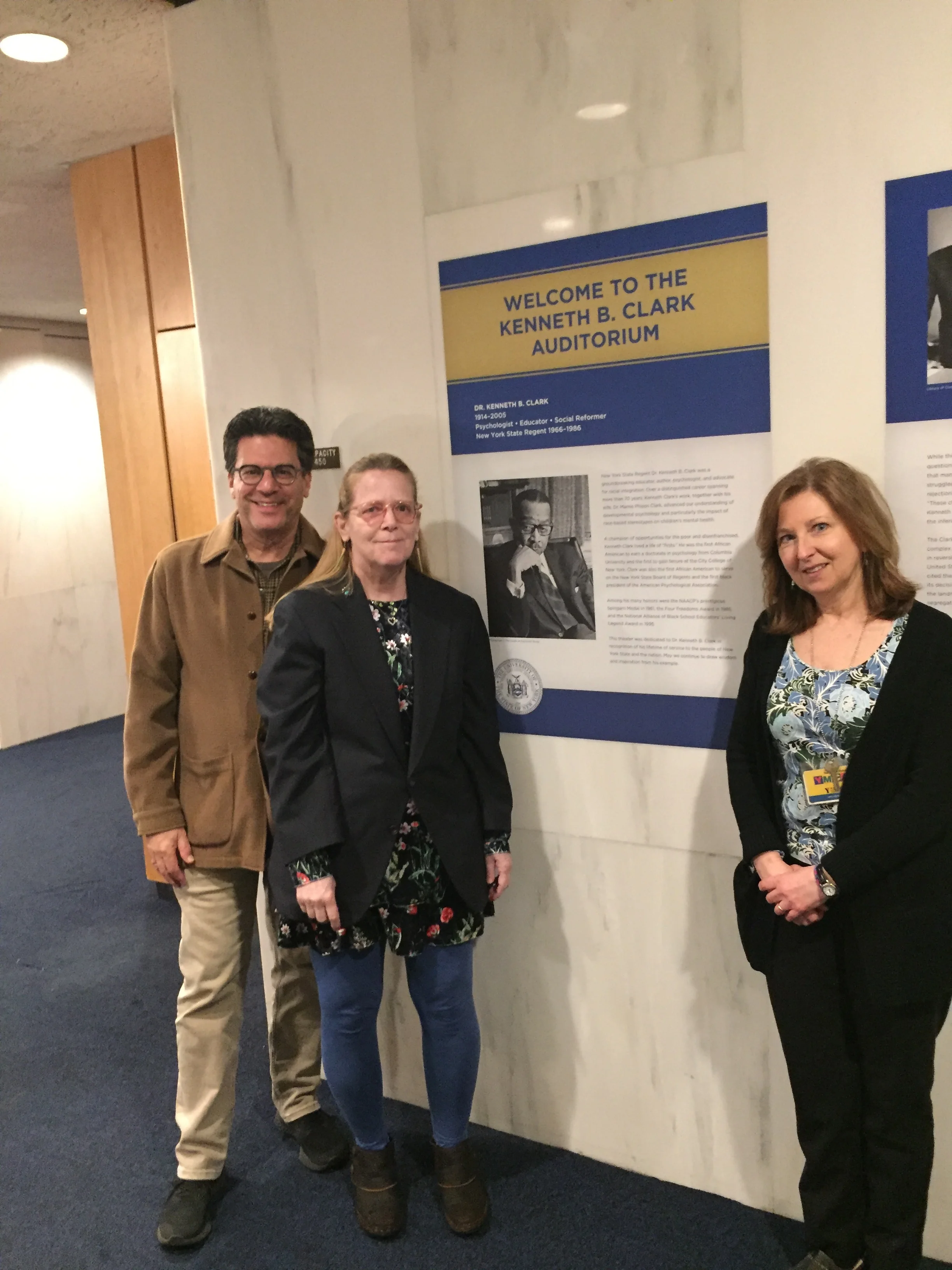 GME Fine Arts Curator David Deitch, with Carla Borea (daughter of and heir to the Estate of photographer Raimondo Borea) and Nancy Kelley, New York State Museum Director of Museum Support Services in front of wall text including Raimondo Borea’s photograph of Kenneth B. Clark.