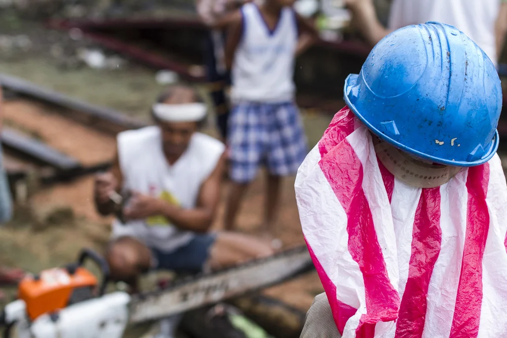 A boy watches adults cleaning a chainsaw they will use to cut boards out of scrap wood and begin rebuilding permanent houses - in Veloso, Samar. The relief team had intended to help the community build temporary shelters but found a town competent and ready to rebuild their homes right away. 