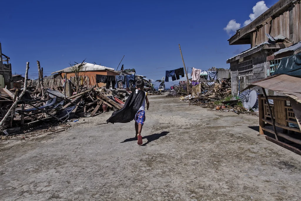A caped boy runs between piles of wreckage in a street in Marabut City, Samar.