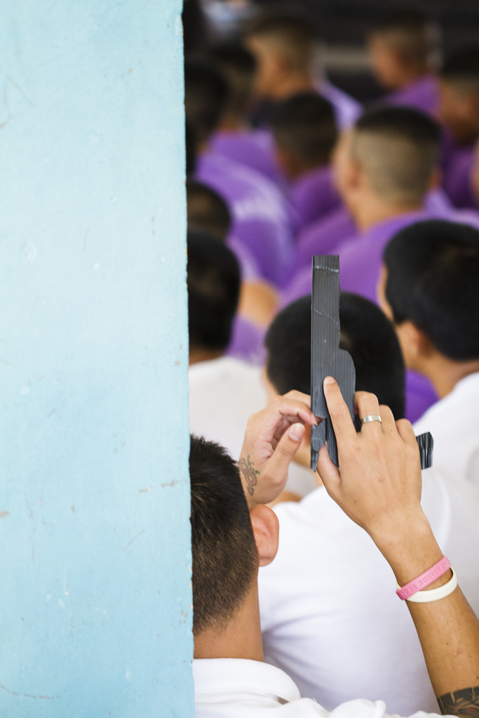 A young man at the Mae Rim Juvenile Correction Facility plays with a cardboard handgun as he listens to the combined team from Radical Grace and Sports Friends, Thailand talk about the importance of healthy relationships and good decision-making.