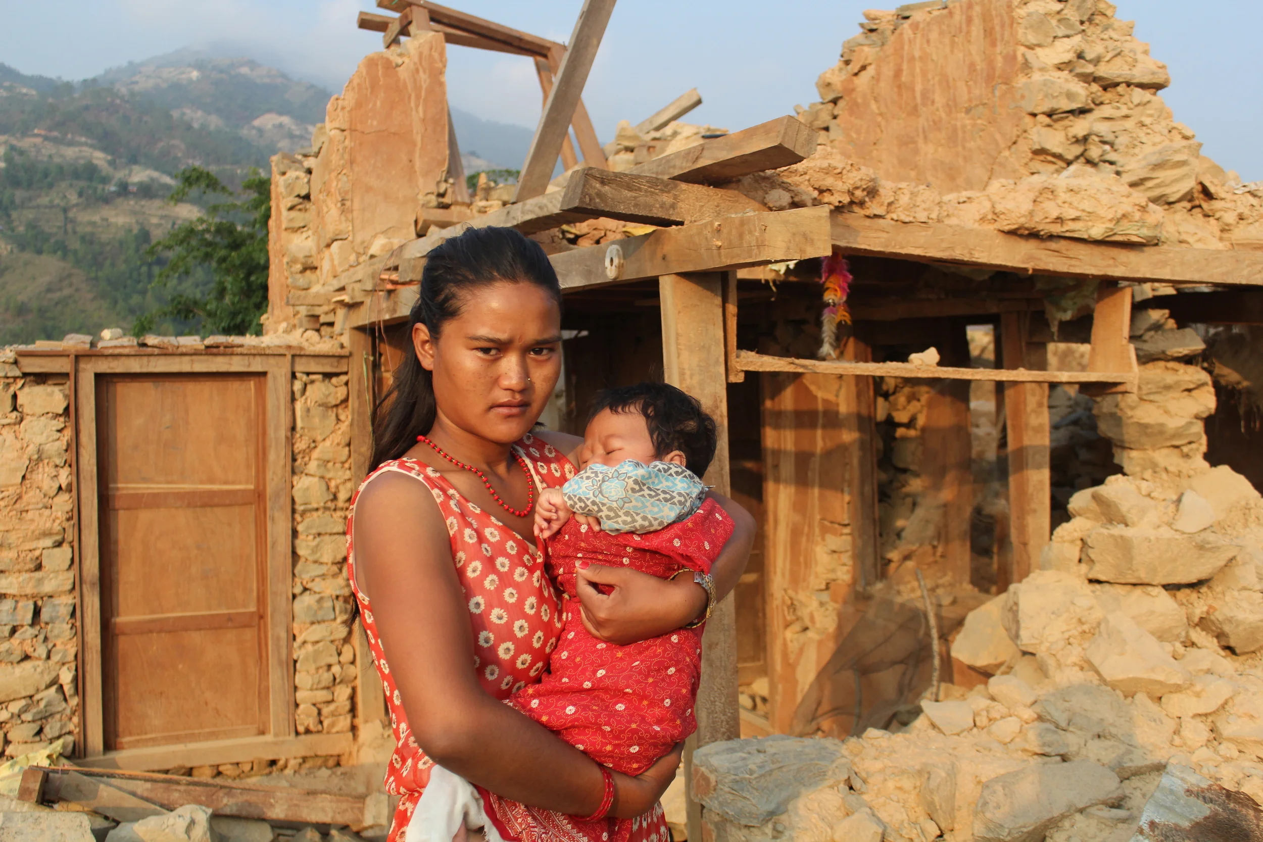 Suraj with his mother in front of the ruins of their house - Photo courtesy of UMN. 