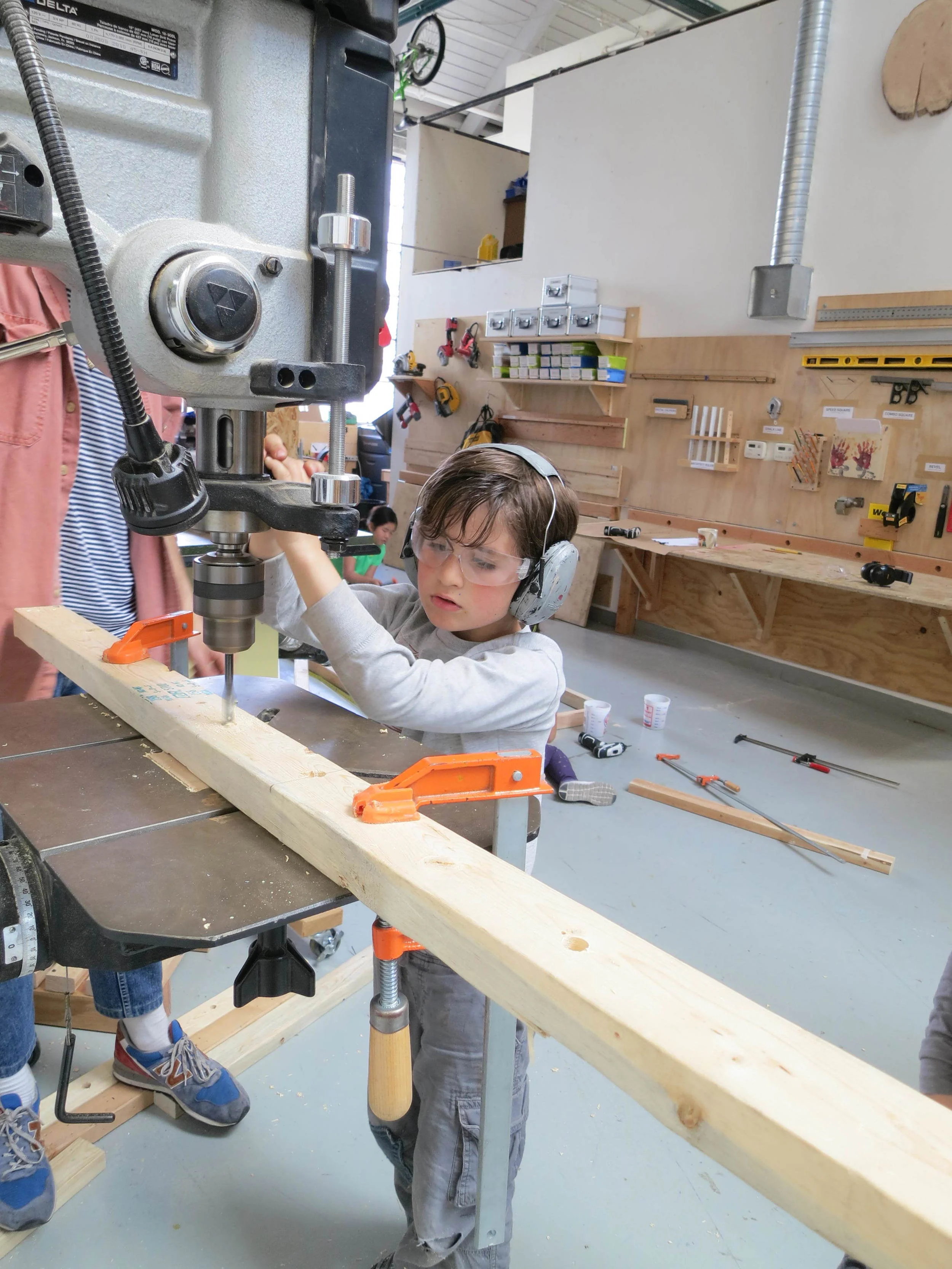 Isaac uses the drill press to make large diameter holes for the Ring Toss project.